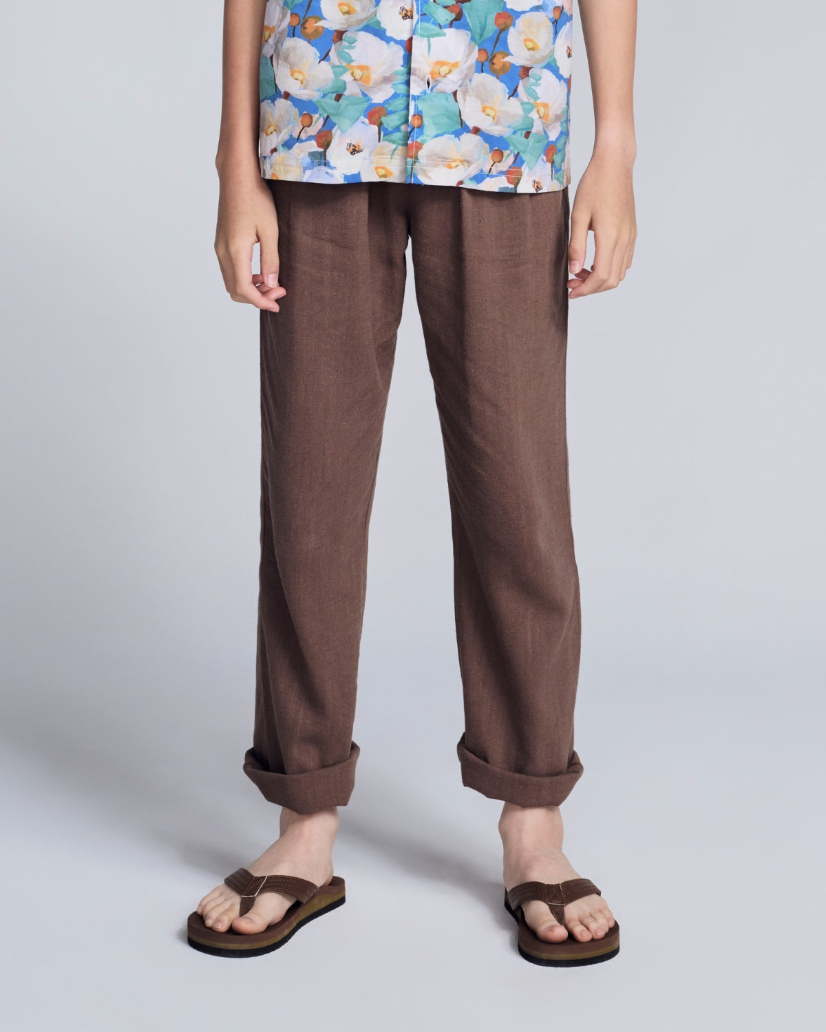 Boy wearing a floral top and brown pants on a light gray background