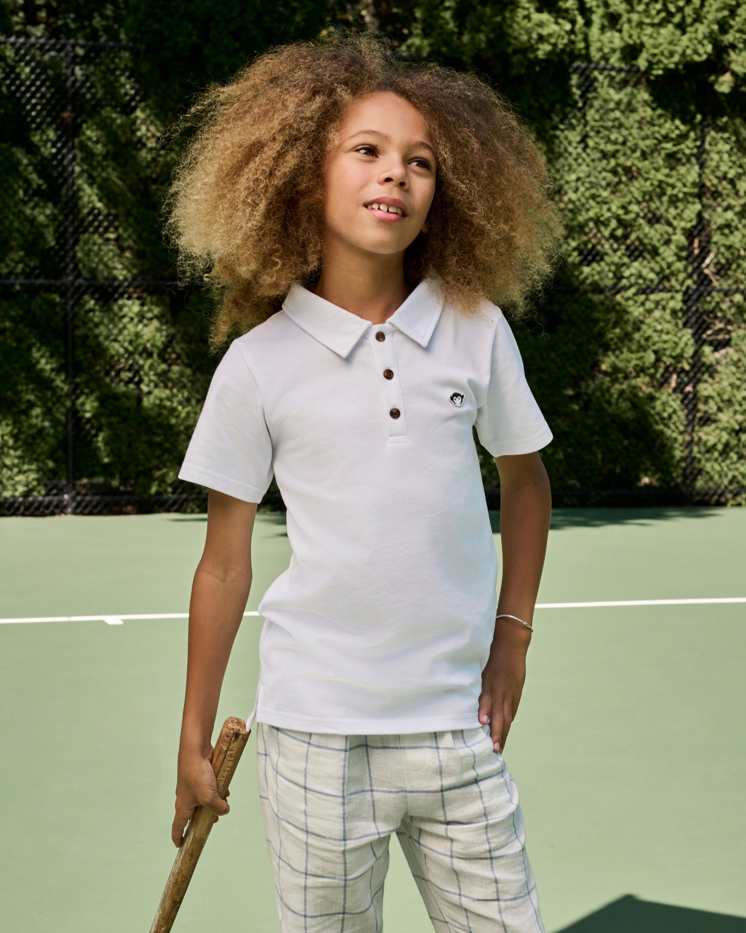 Child wearing a white polo shirt with brown buttons on a tennis court