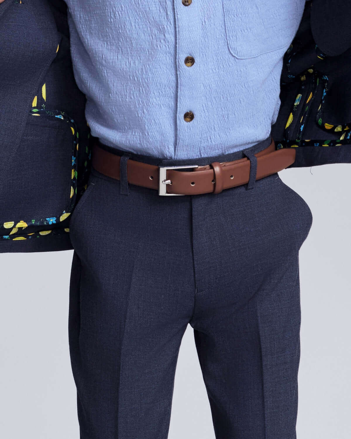 Person wearing a blue shirt, dark pants, and a brown belt with a white background