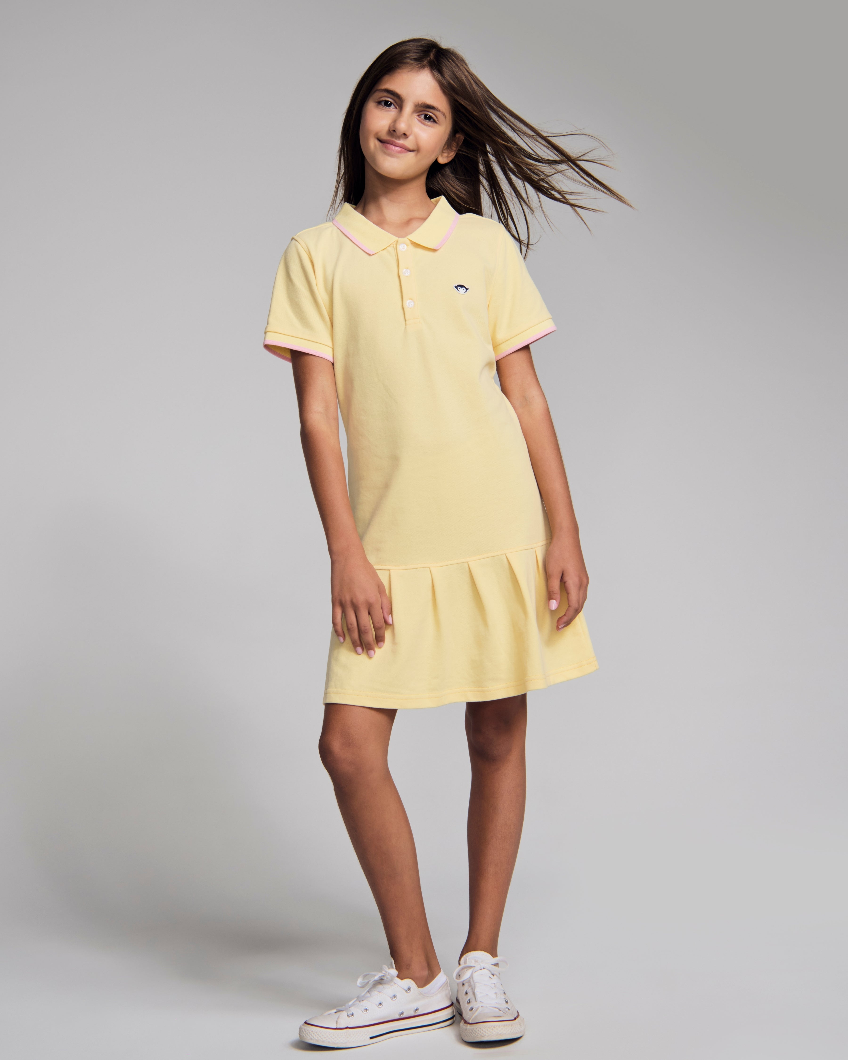 Girl wearing Buttercup Polo Pleated Dress in yellow with short sleeves and pleated skirt.