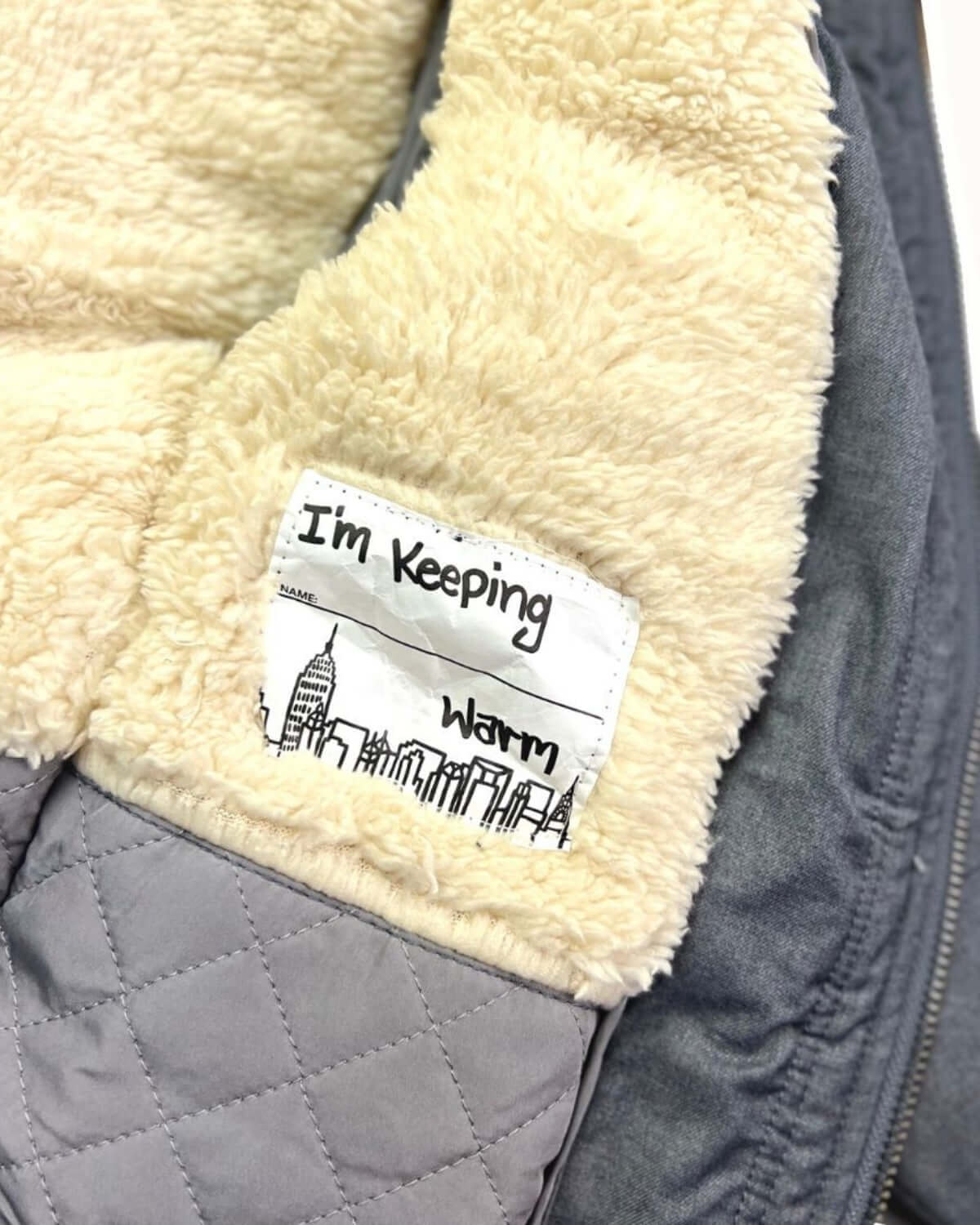 Inside view of the Grey Denali Down Coat showing the sherpa lining and label stating "I'm Keeping Warm".