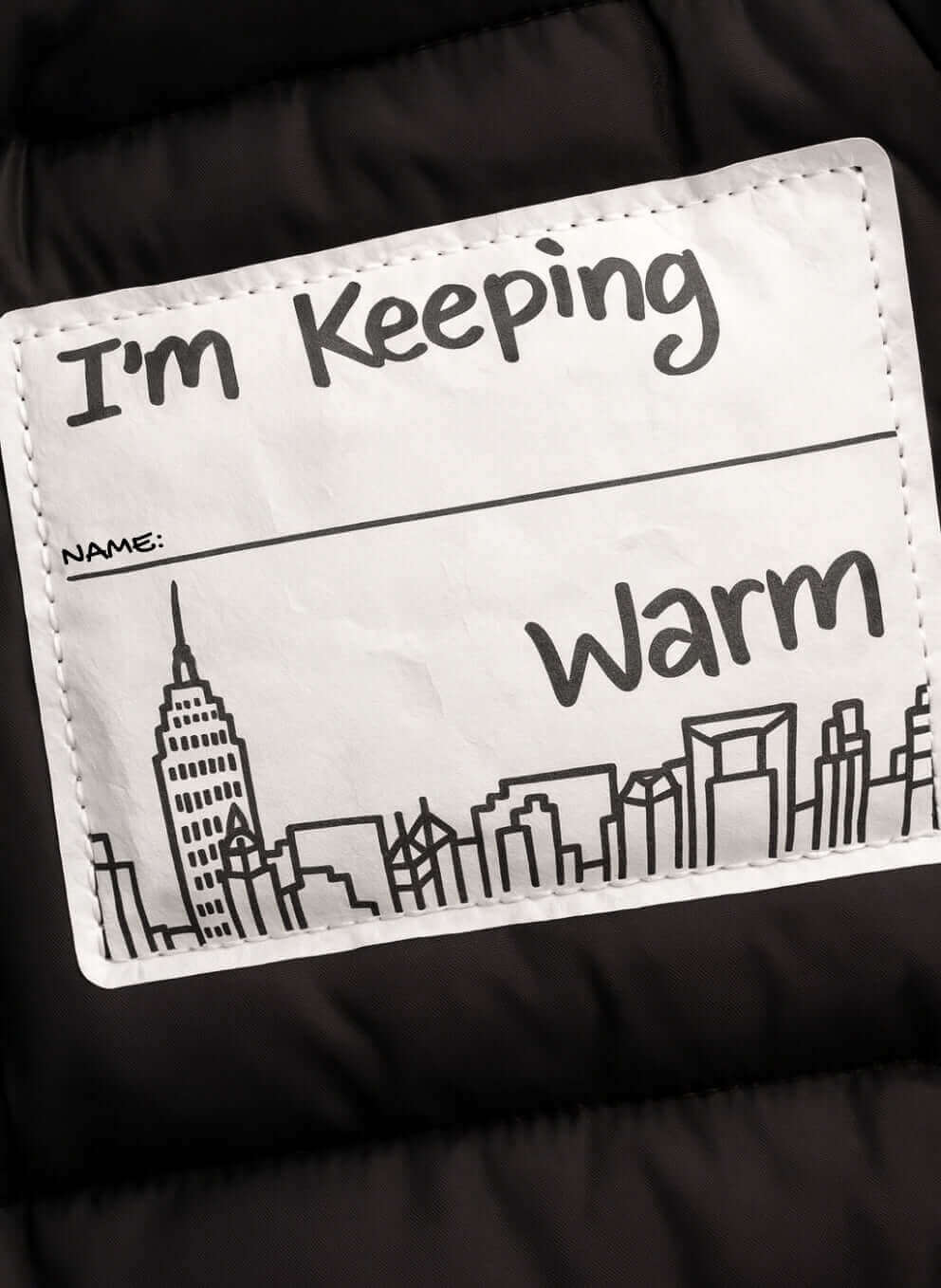 Label on Glitter Black Slim Puffy Coat stating 'I'm Keeping Warm' with city skyline illustration.