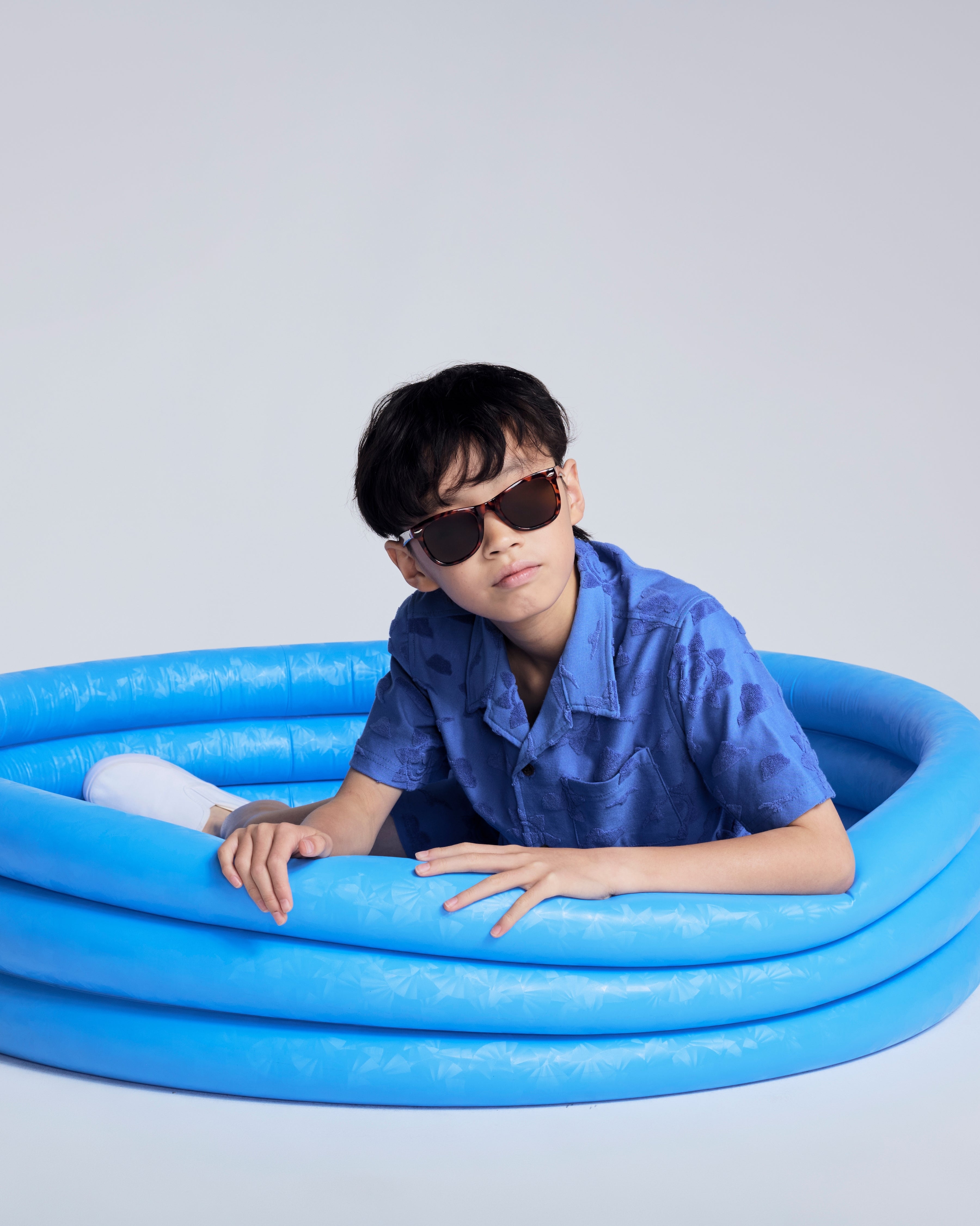 Boy wearing Cobalt Blue Terry Resort Shirt in a blue inflatable pool, stylish and ready for summer fun.