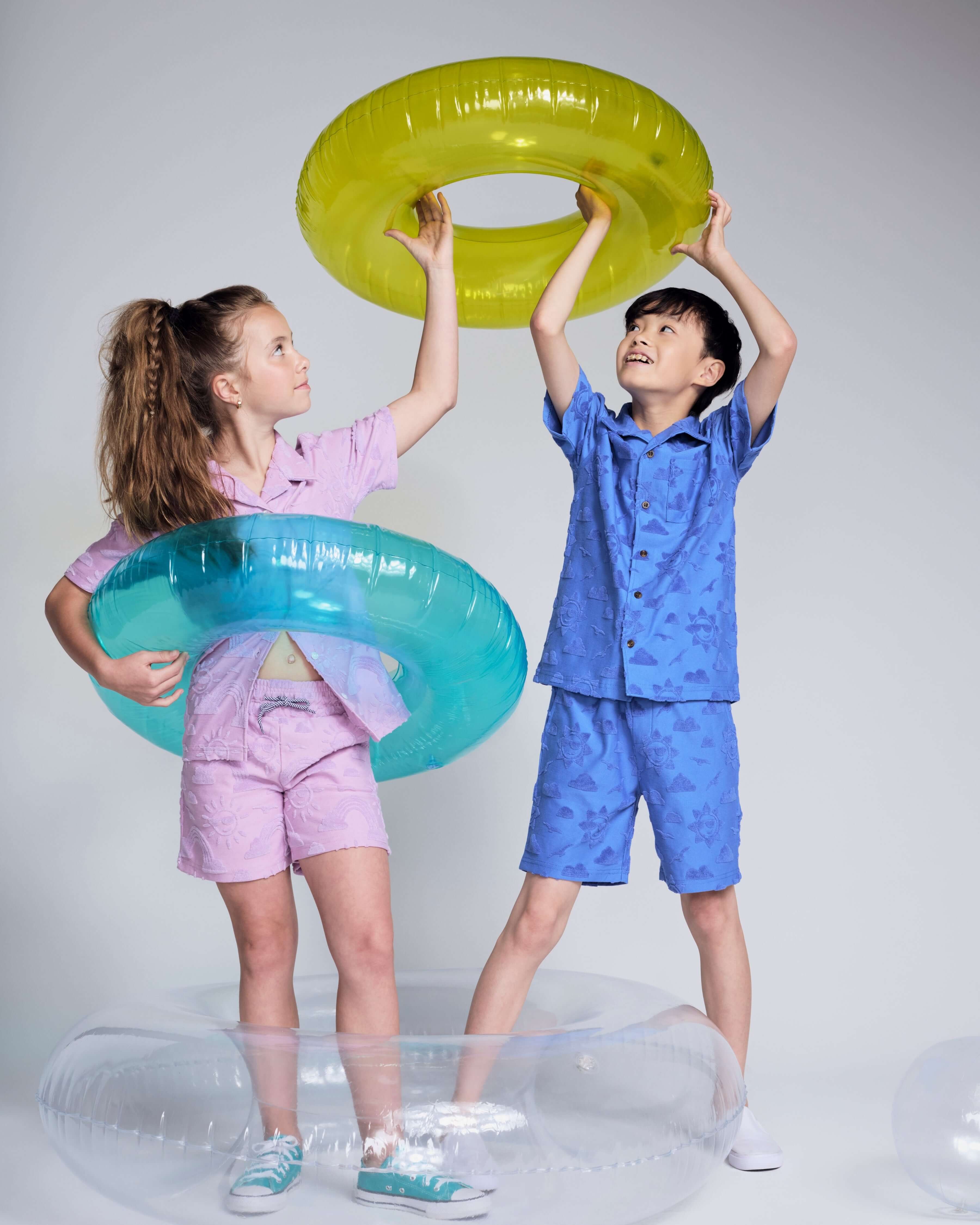 Children holding colorful pool floaties, wearing matching Cobalt Blue Terry Resort Short and playful resort attire.