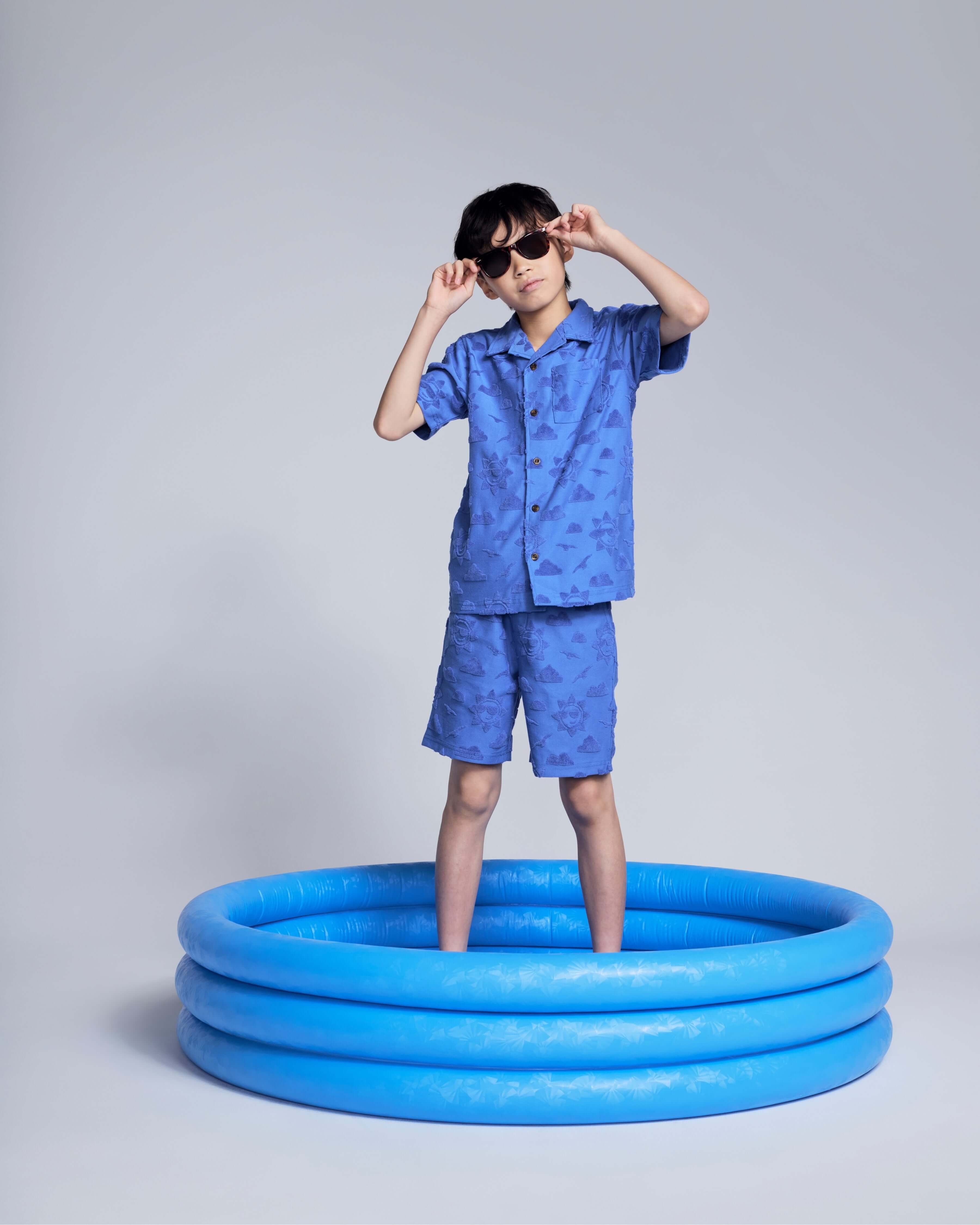 Cobalt Blue Terry Resort Short worn by a boy standing in a blue inflatable pool, wearing sunglasses and a matching shirt.