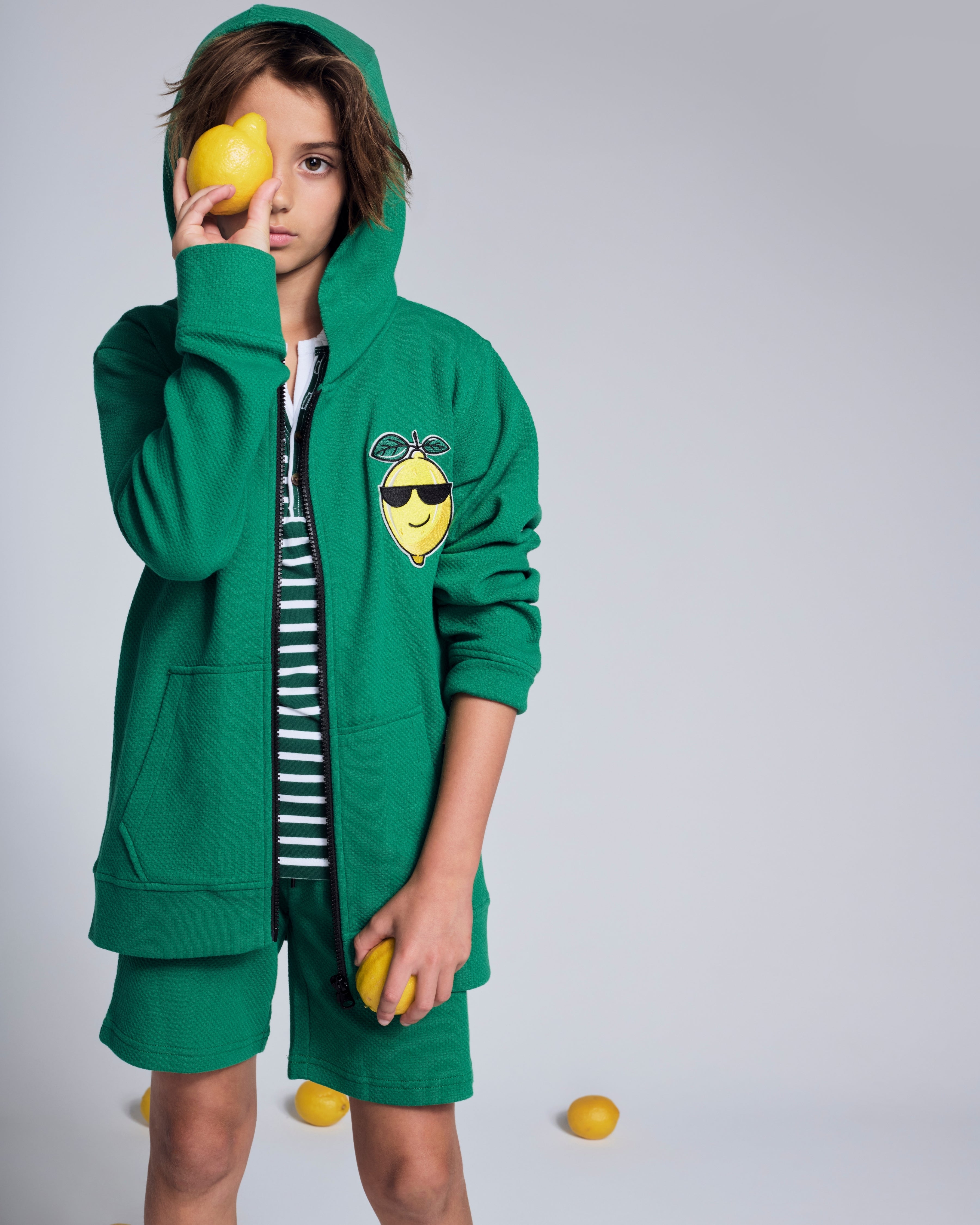 Boy wearing a green Cool Lemon Strivers Hoodie with a lemon graphic patch, holding a lemon.