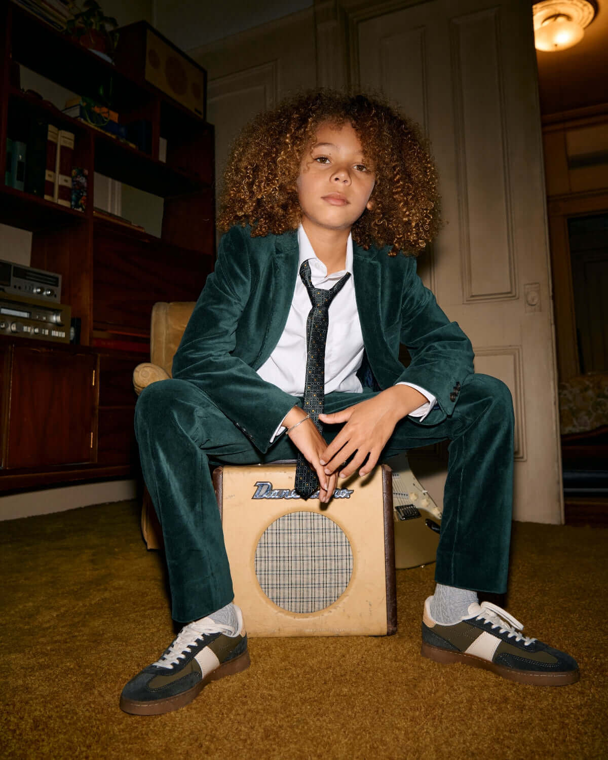 Kid wearing an Evergreen Velvet Blazer and stylish shoes, posing confidently with an amplifier.