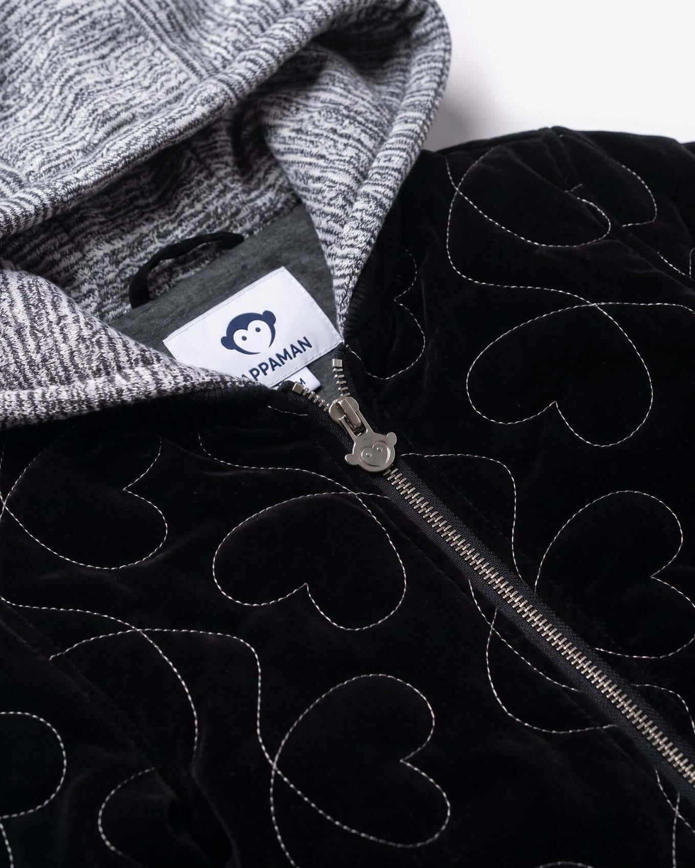 Close-up of a black jacket with heart patterns and a gray hood, featuring a brand label.