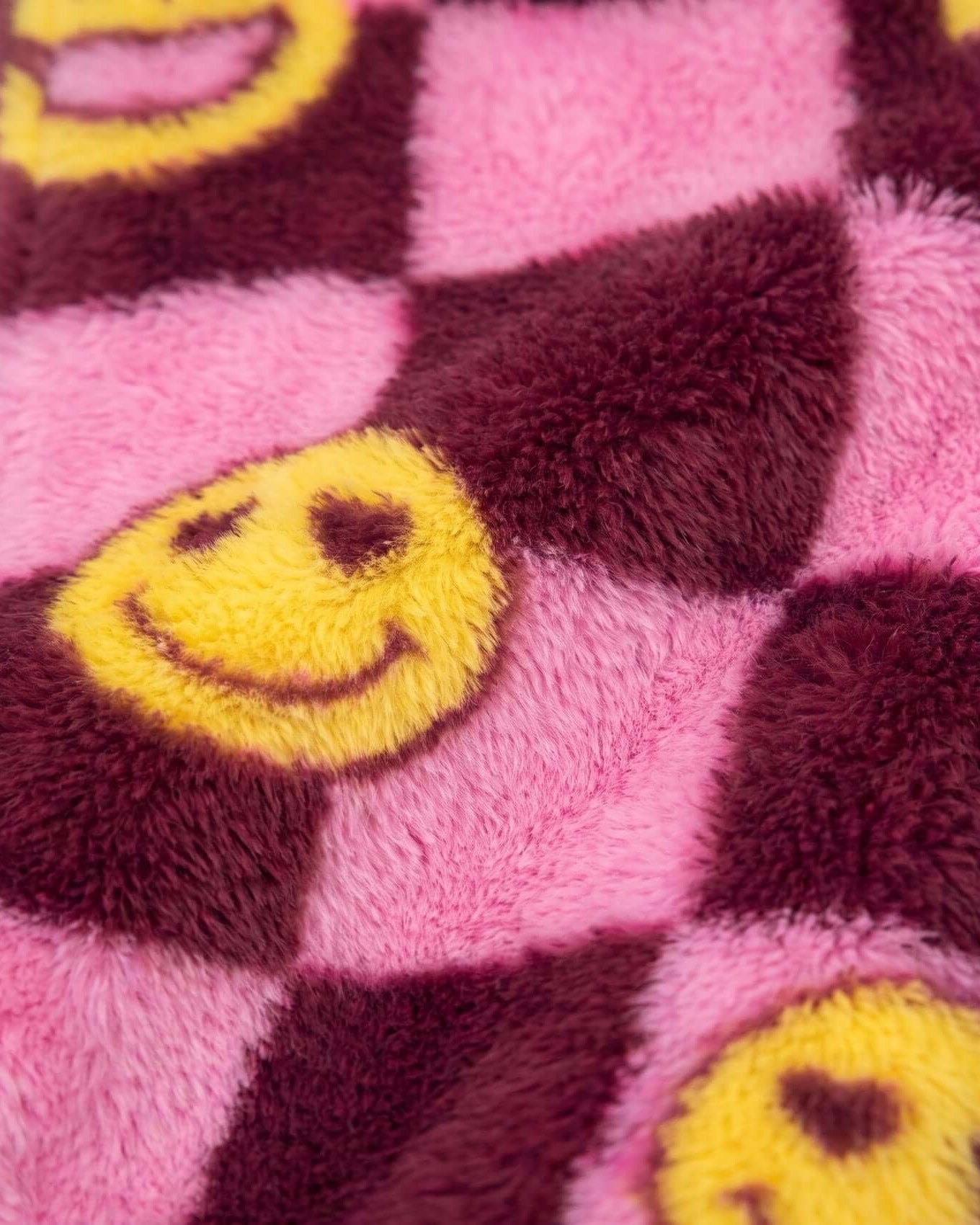 Close-up of a pink and purple checkered fabric with yellow smiley face patches.
