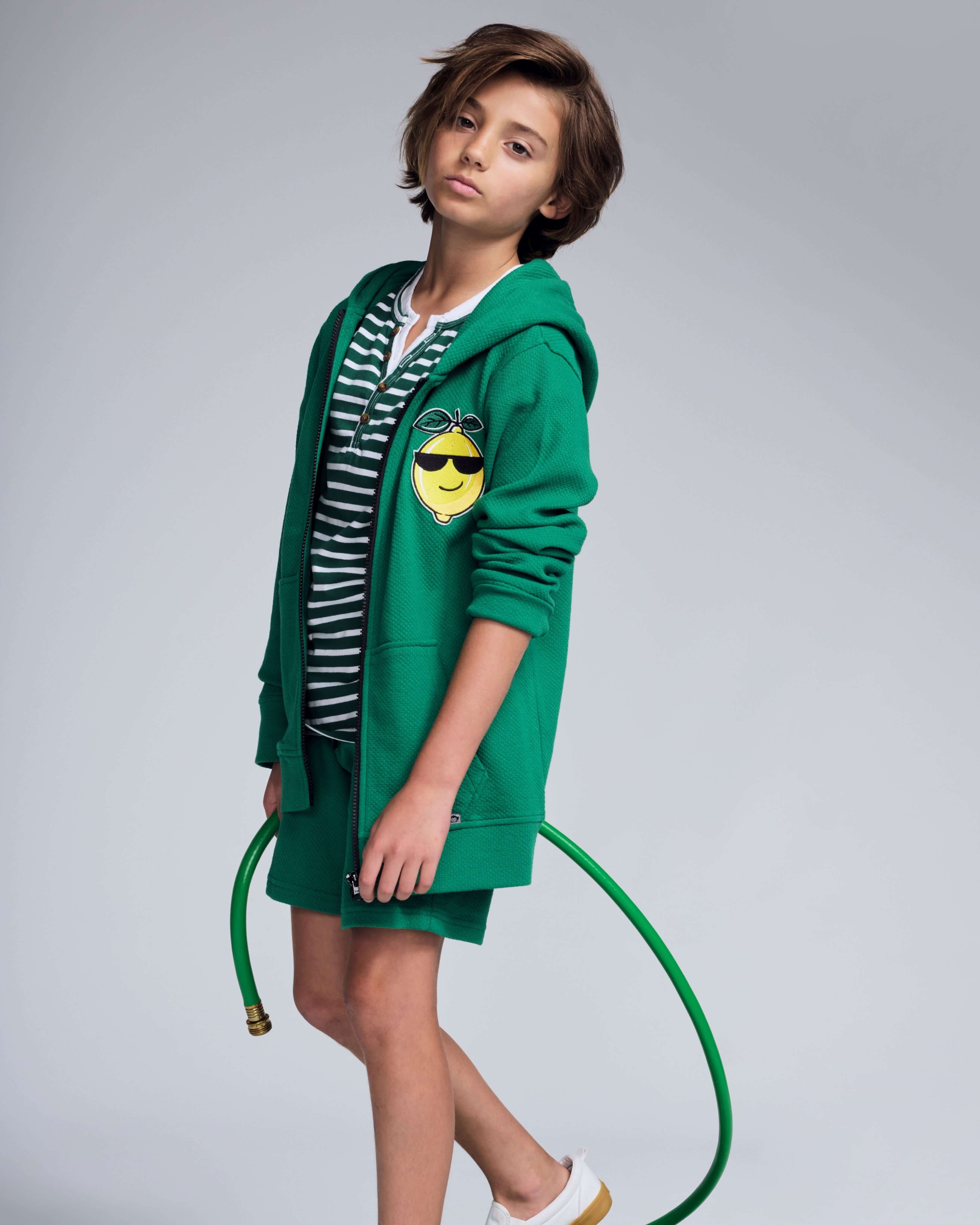 Boy wearing a Garden Green Resort Short with a green hoodie and striped shirt, holding a garden hose.