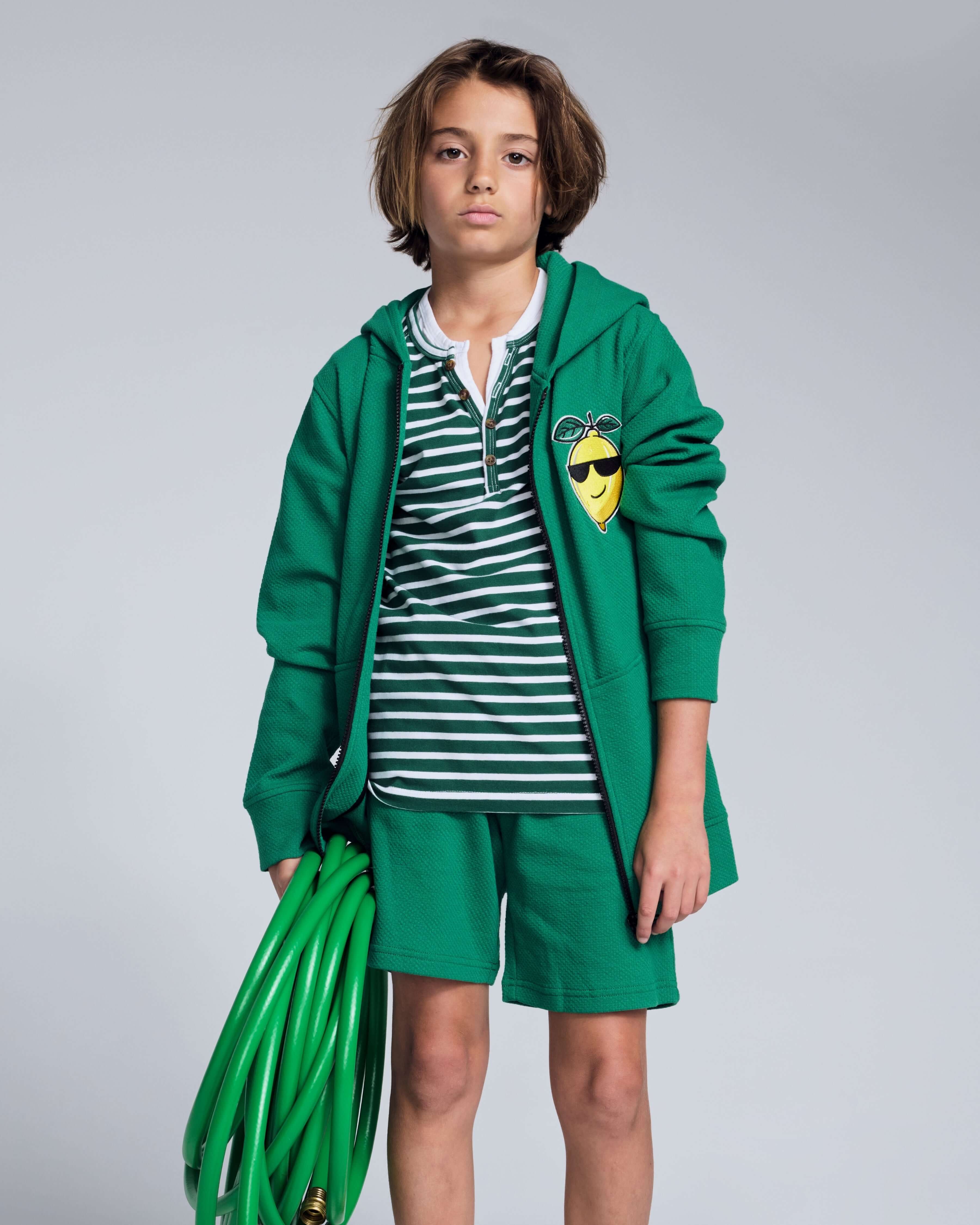 Child wearing a green hoodie and Garden Green Stripe Hilltop Henley with a garden hose.