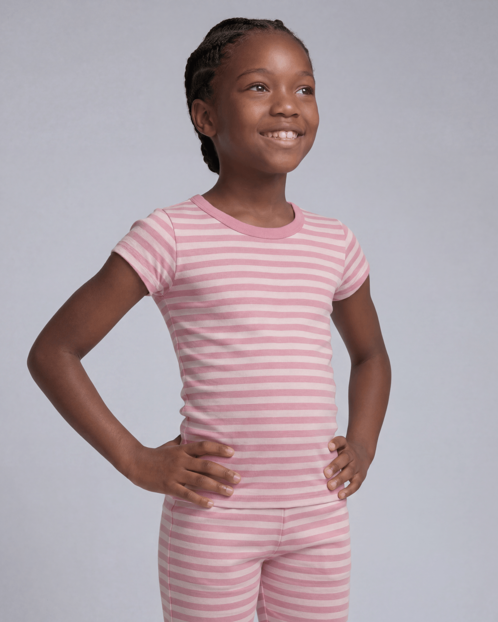 Young girl wearing pink striped pajamas against a gray background