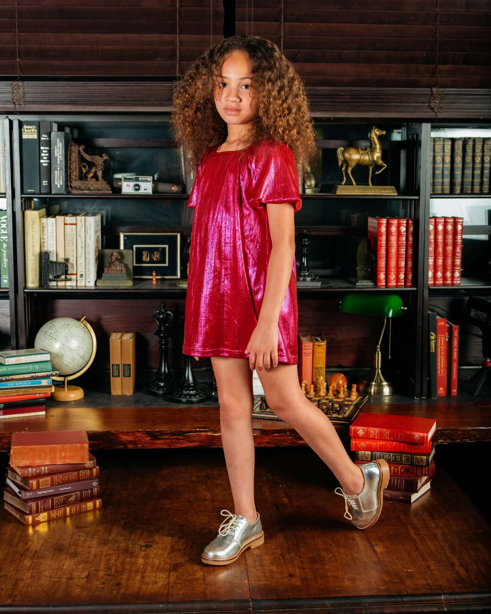 A young girl wearing the Fuchsia Emma Dress featuring shiny puff sleeves and a square neckline in a stylish setting.