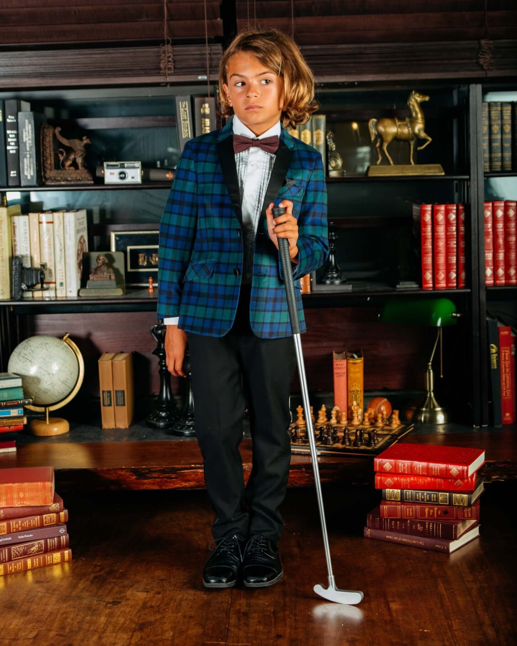 A child in a Blackwatch Velvet Plaid Tuxedo Suit Jacket poses with a golf club, showcasing a stylish formal look.