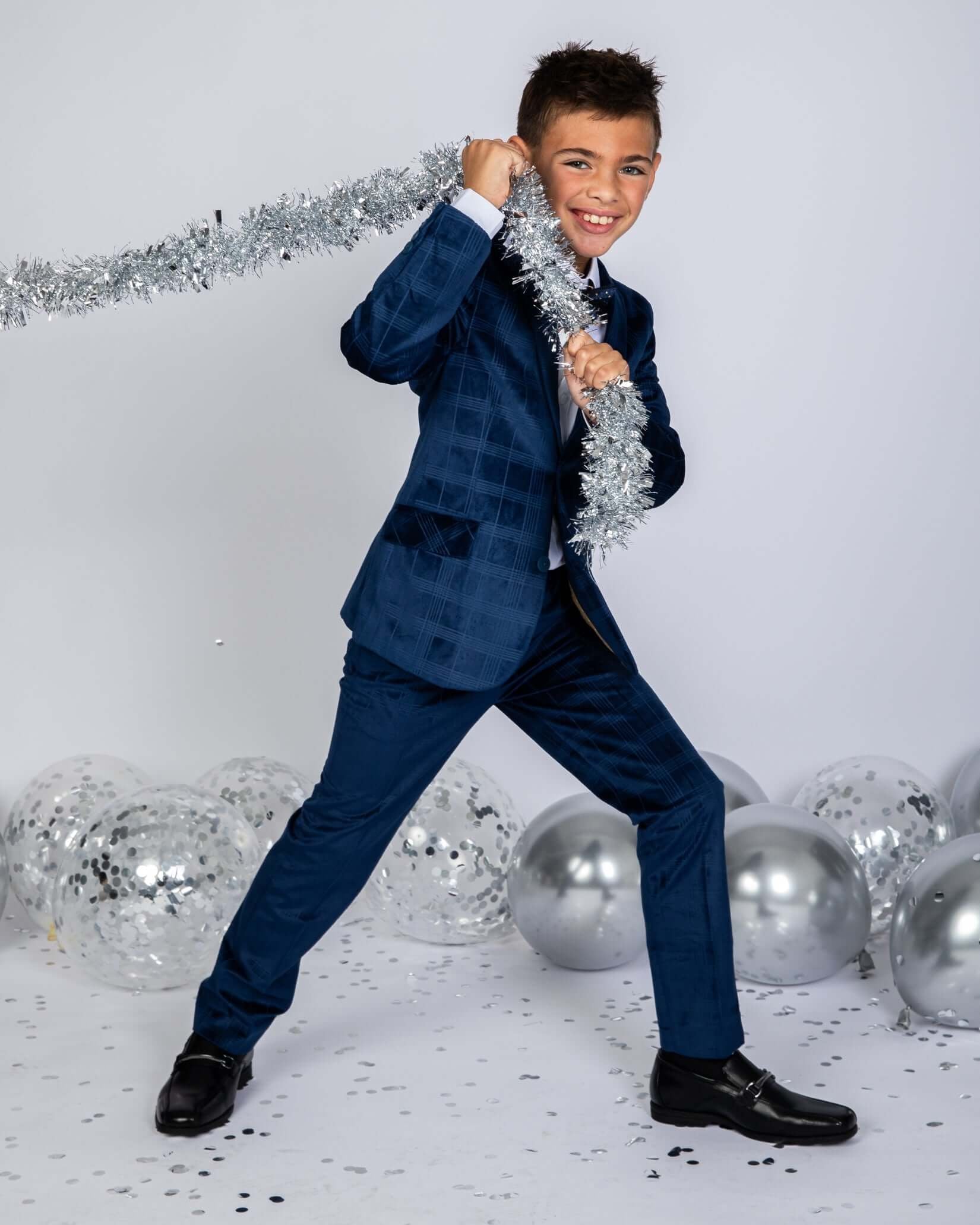 Boy wearing a Blue Velvet Suit Blazer, celebrating with silver tinsel and surrounded by party decorations.