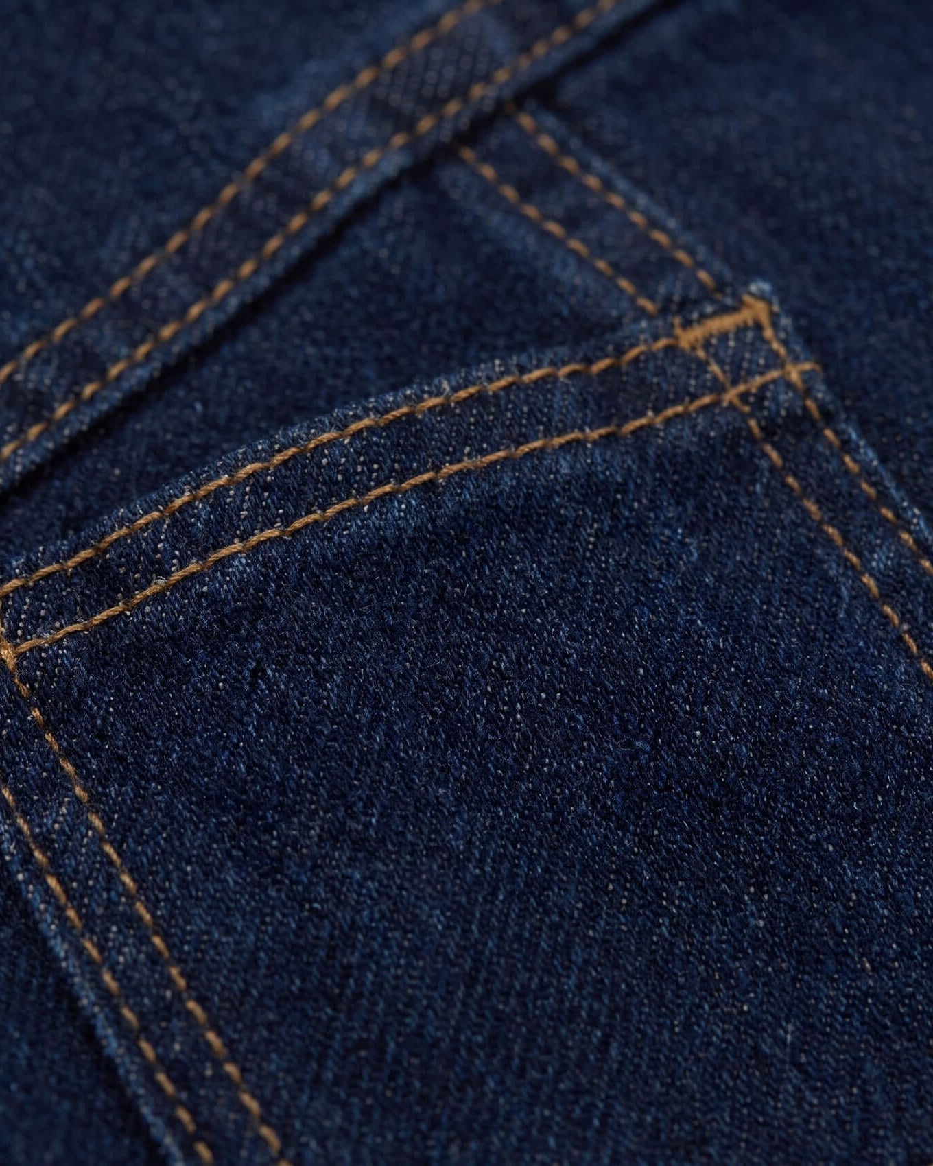 Close-up of blue denim fabric with brown stitching