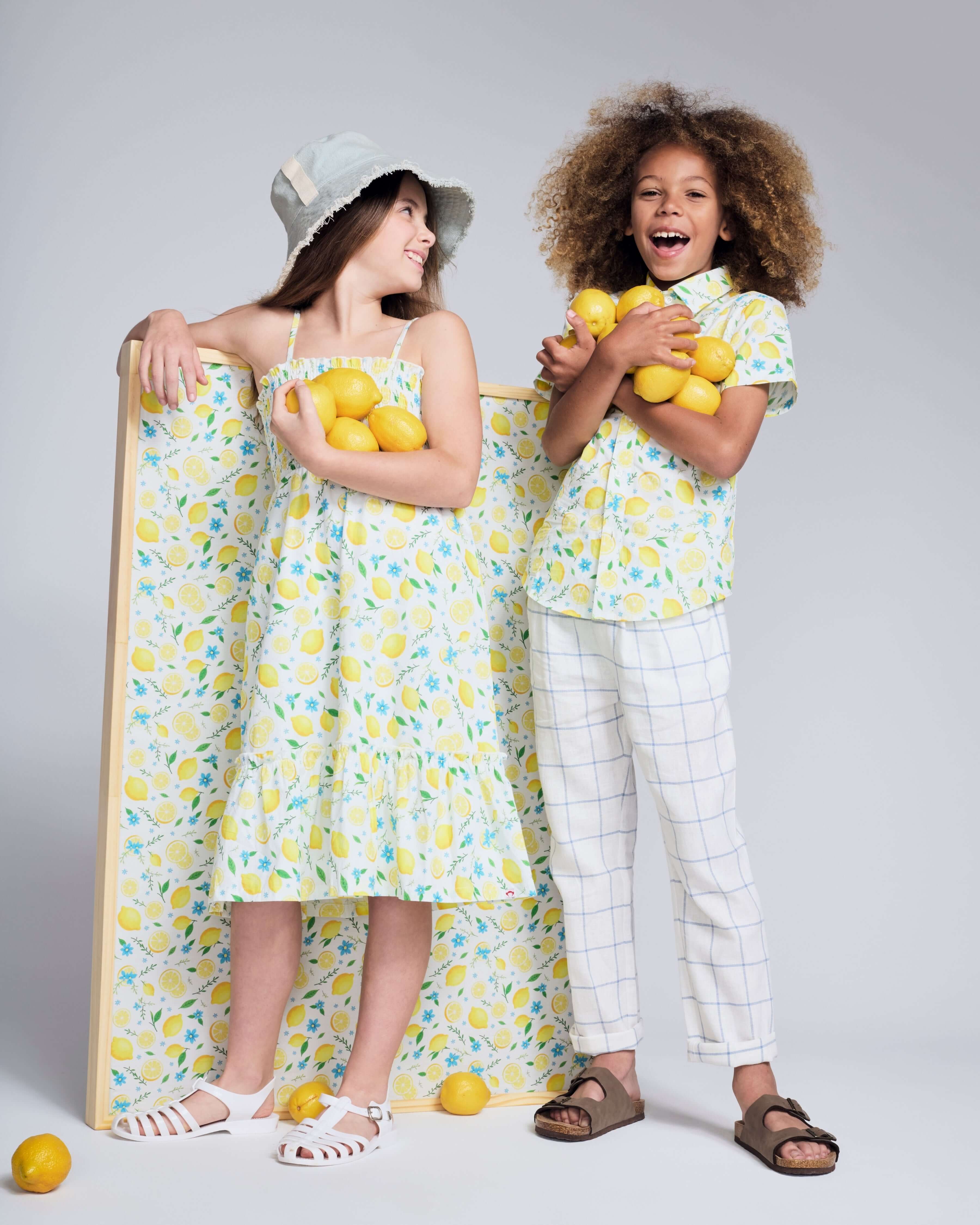 Two kids in a Lemon Zest Day Party Shirt surrounded by lemons, showcasing a fun summer vibe.