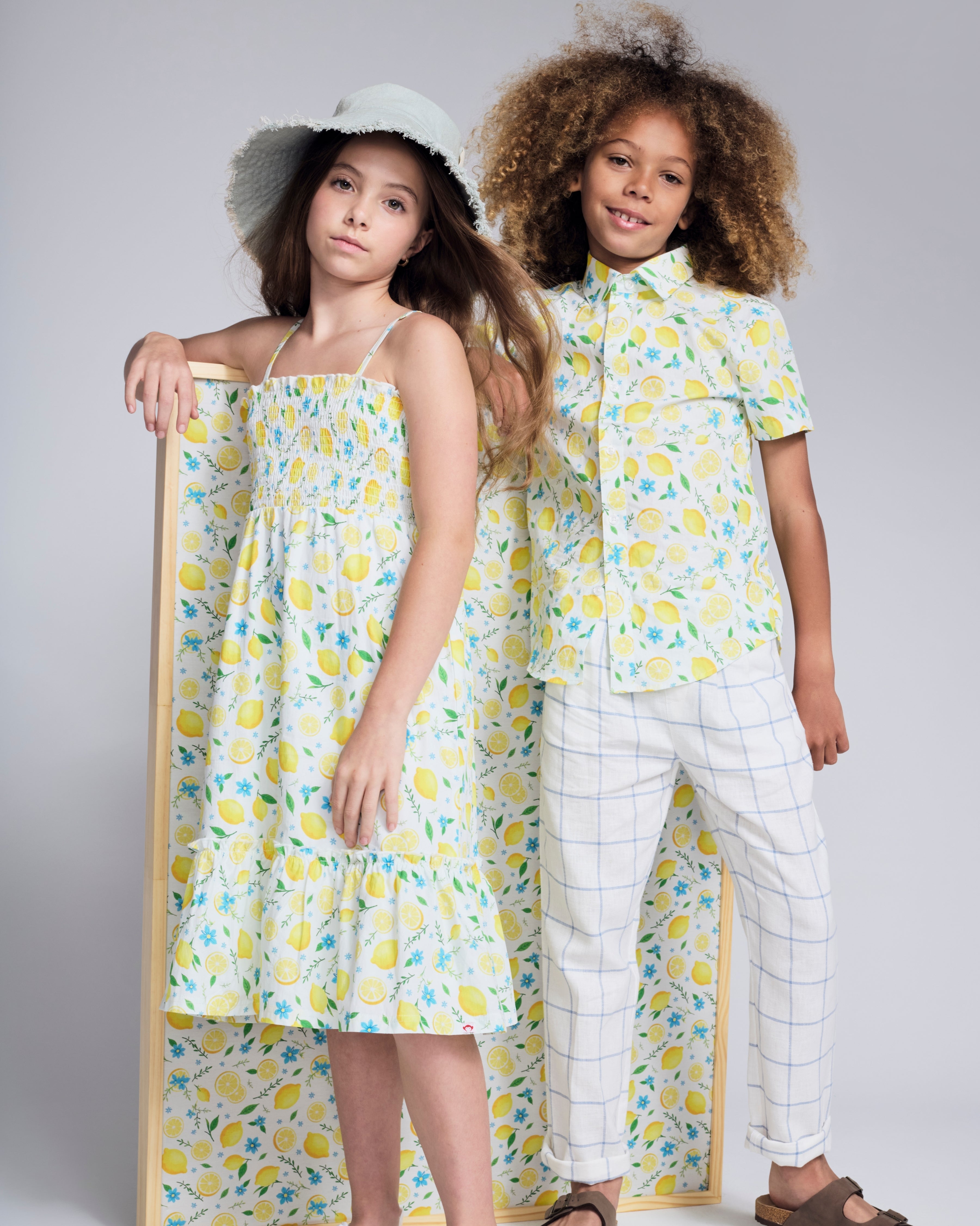 Two children wearing fresh summer outfits with lemon prints, showcasing the Lemon Zest Day Party Shirt.