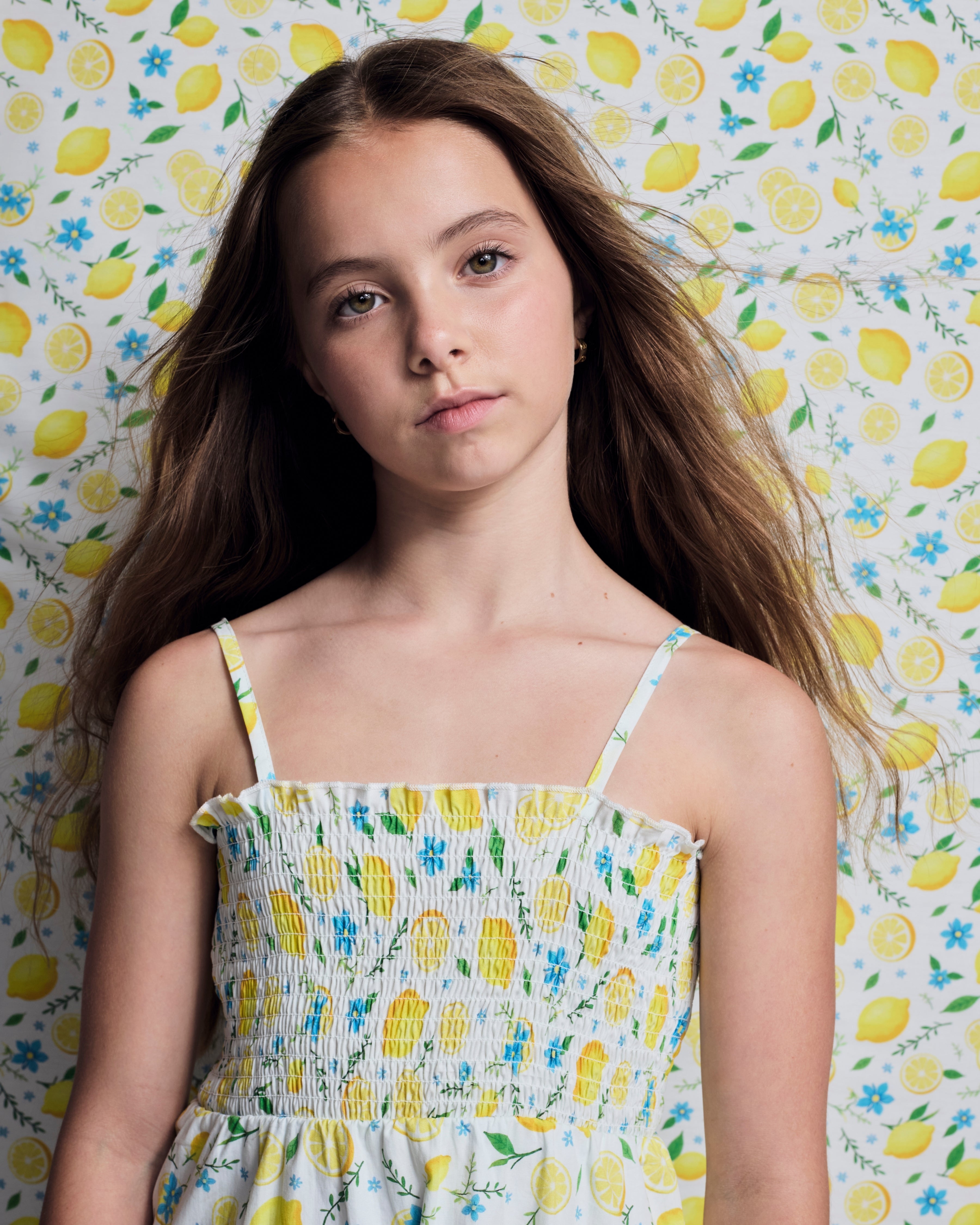 Lemon Zest Madison Dress worn by a girl with long hair, featuring yellow lemon print and ruffle details.