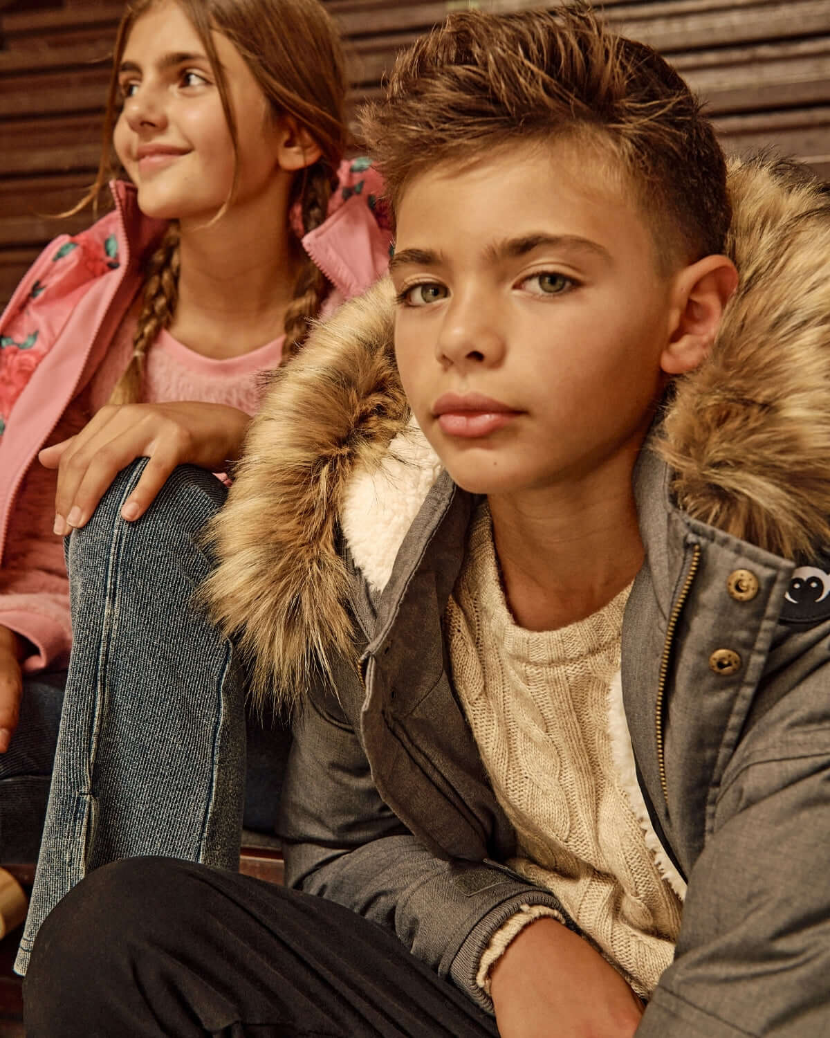 Boy wearing a Grey Denali Down Coat with fur trim and sherpa lining, sitting next to a girl in a pink jacket.