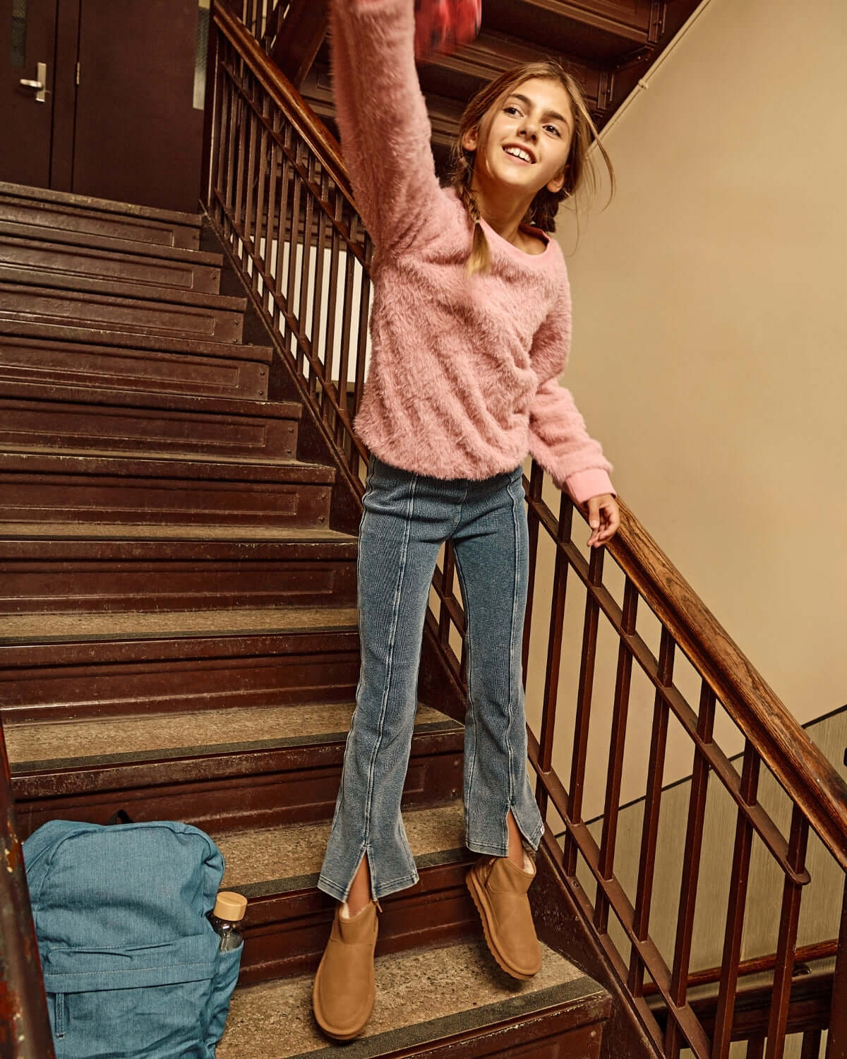 Girl wearing Dusk Blue Flare Leggings and a pink sweater, jumping on stairs, showcasing style and comfort.