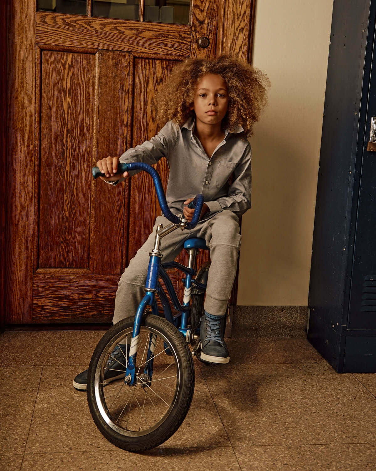 Child wearing Novelty Grey Heather Sideline Sweatpants sitting on a bicycle in a hallway.