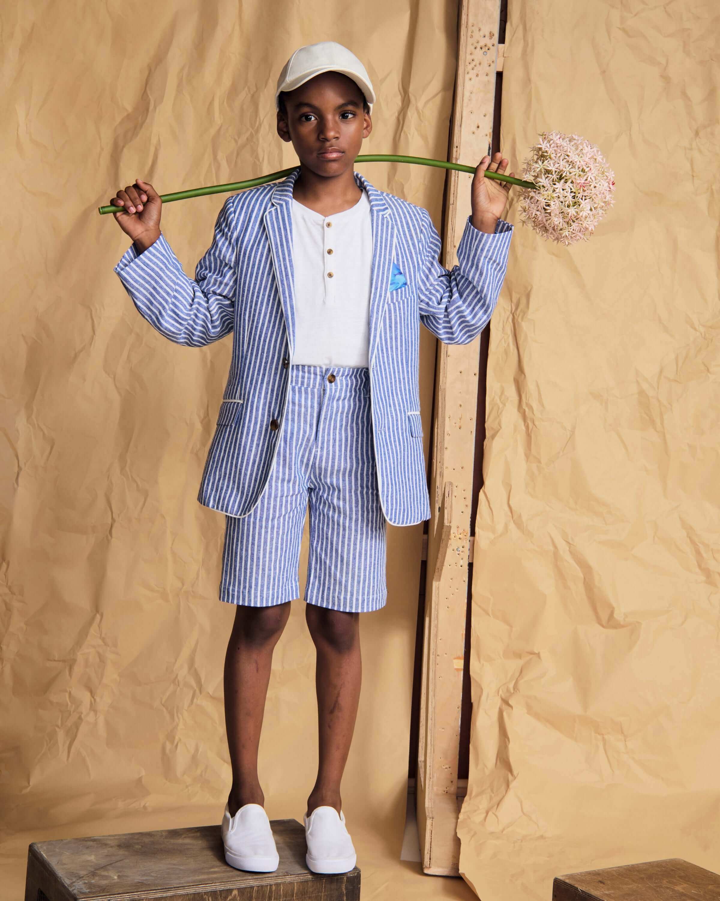 Child wearing a blue striped suit holding a plant against a beige background