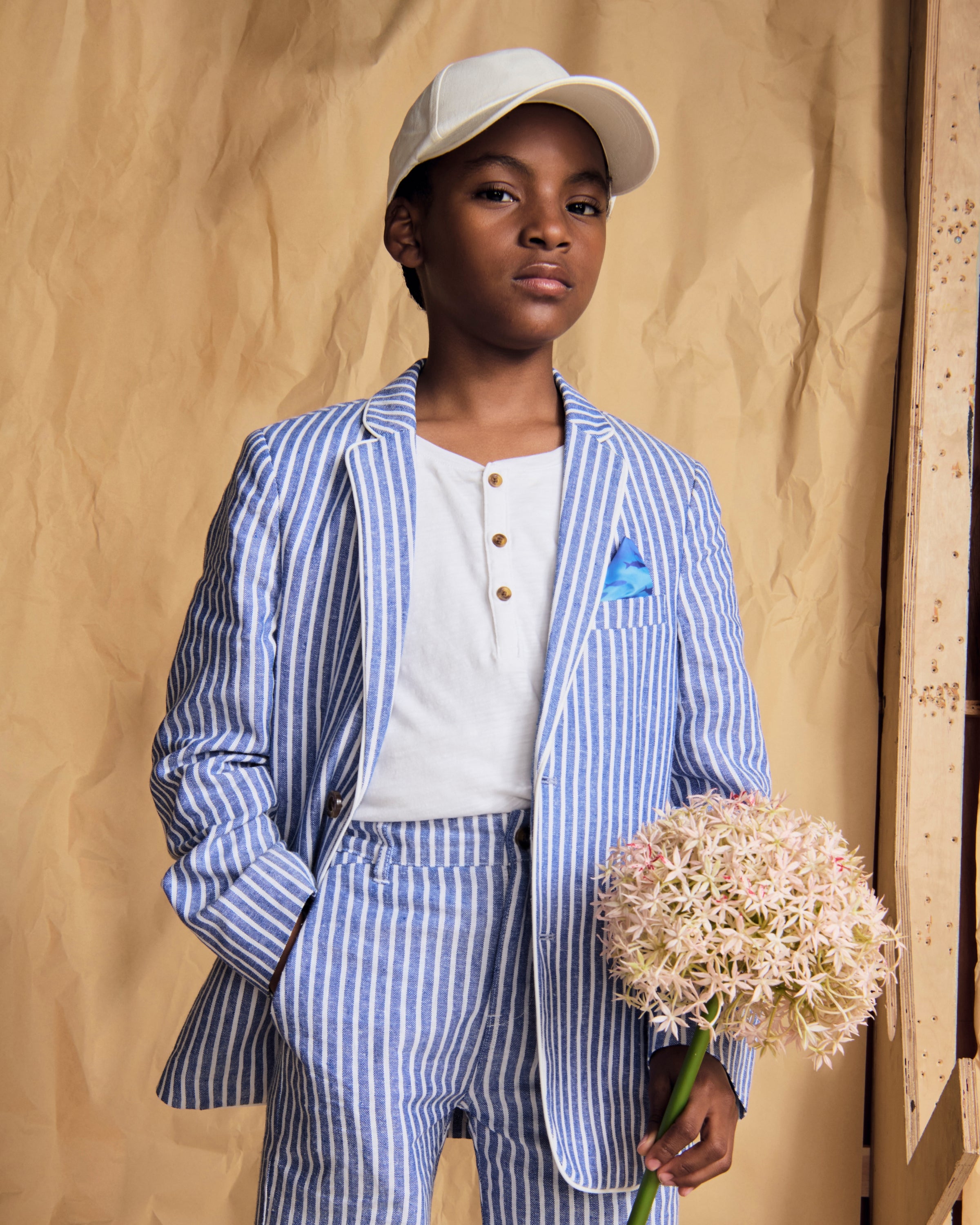 A child wearing a Linen Canopy Stripe Club Blazer and matching trousers, holding flowers for a stylish spring look.