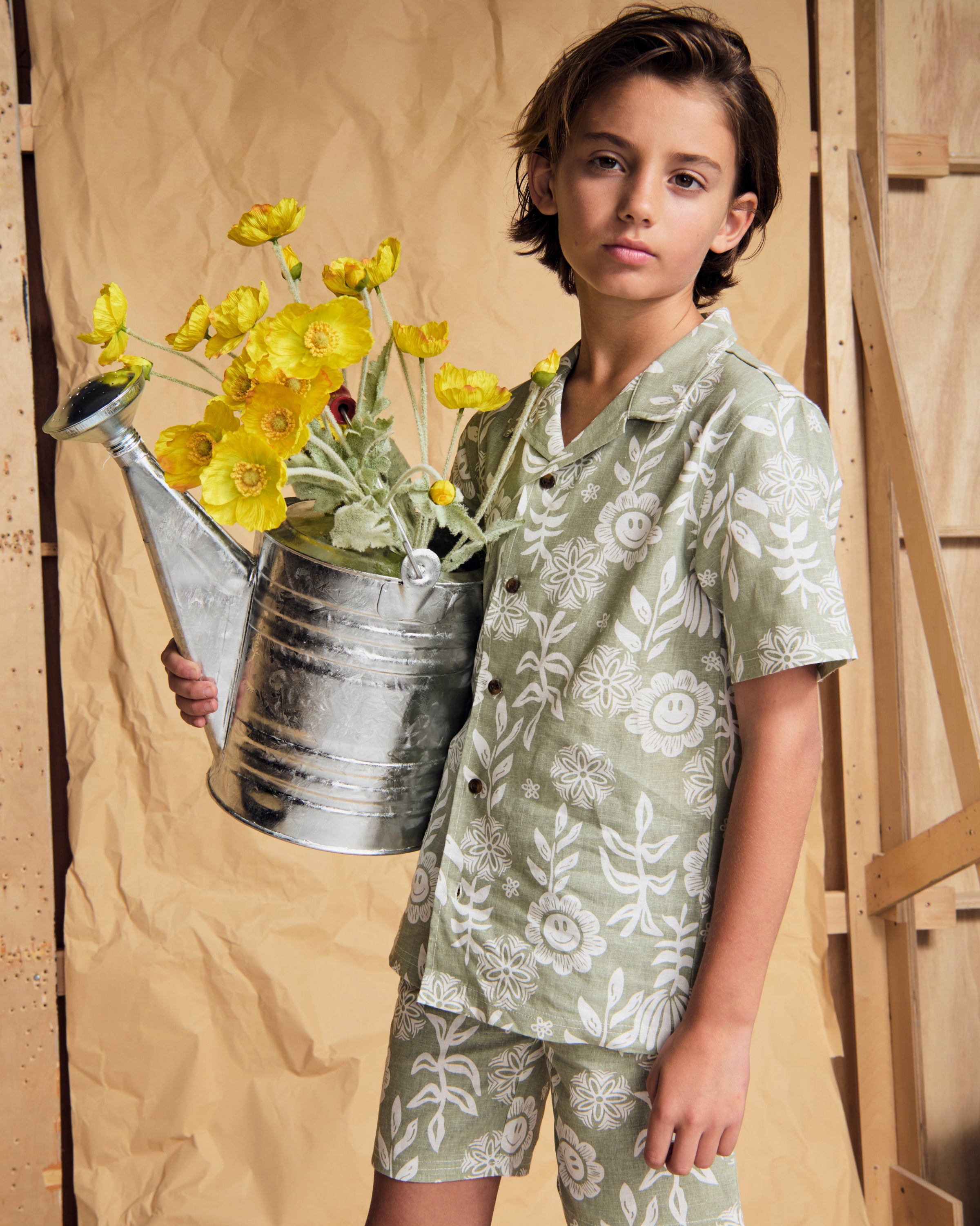 Linen Sage Sunflower Camp Collar Shirt worn by a child holding a watering can filled with yellow flowers.