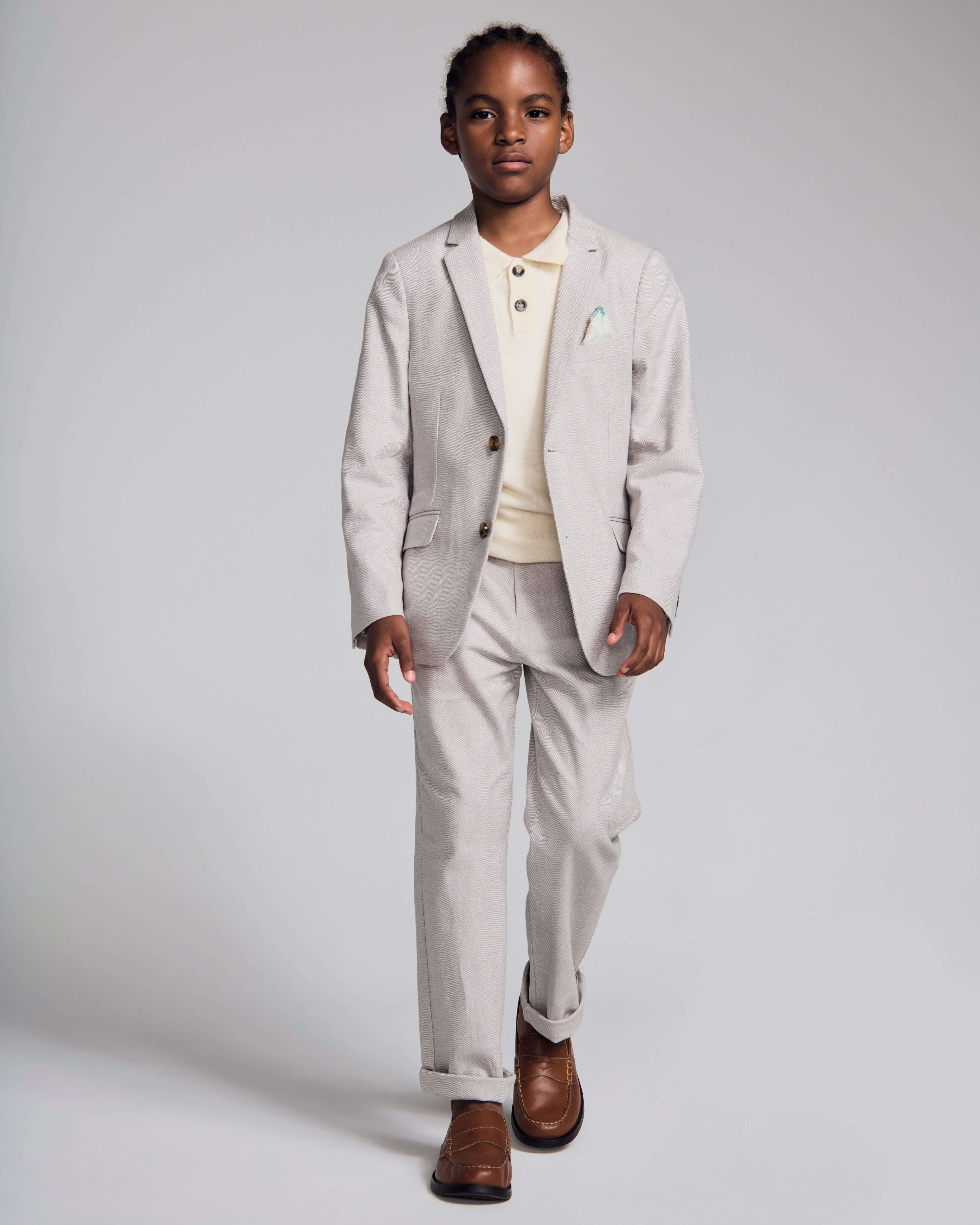 A boy wearing a Linen Warm Grey Sports Jacket paired with light pants and a polo, perfect for spring occasions.