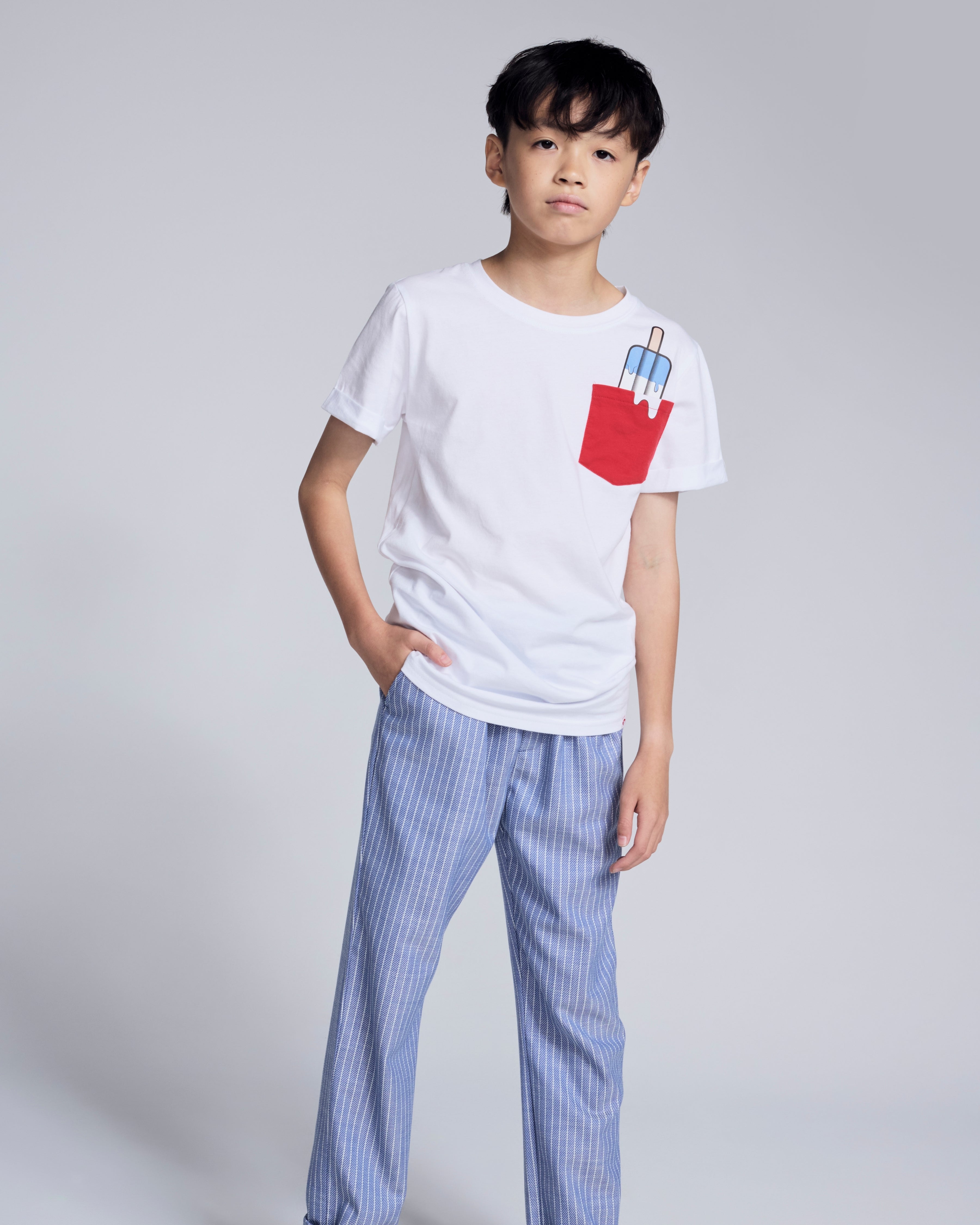 A boy wearing a white t-shirt with a red pocket and Nautical Stripe Resort Pant featuring blue and white stripes.