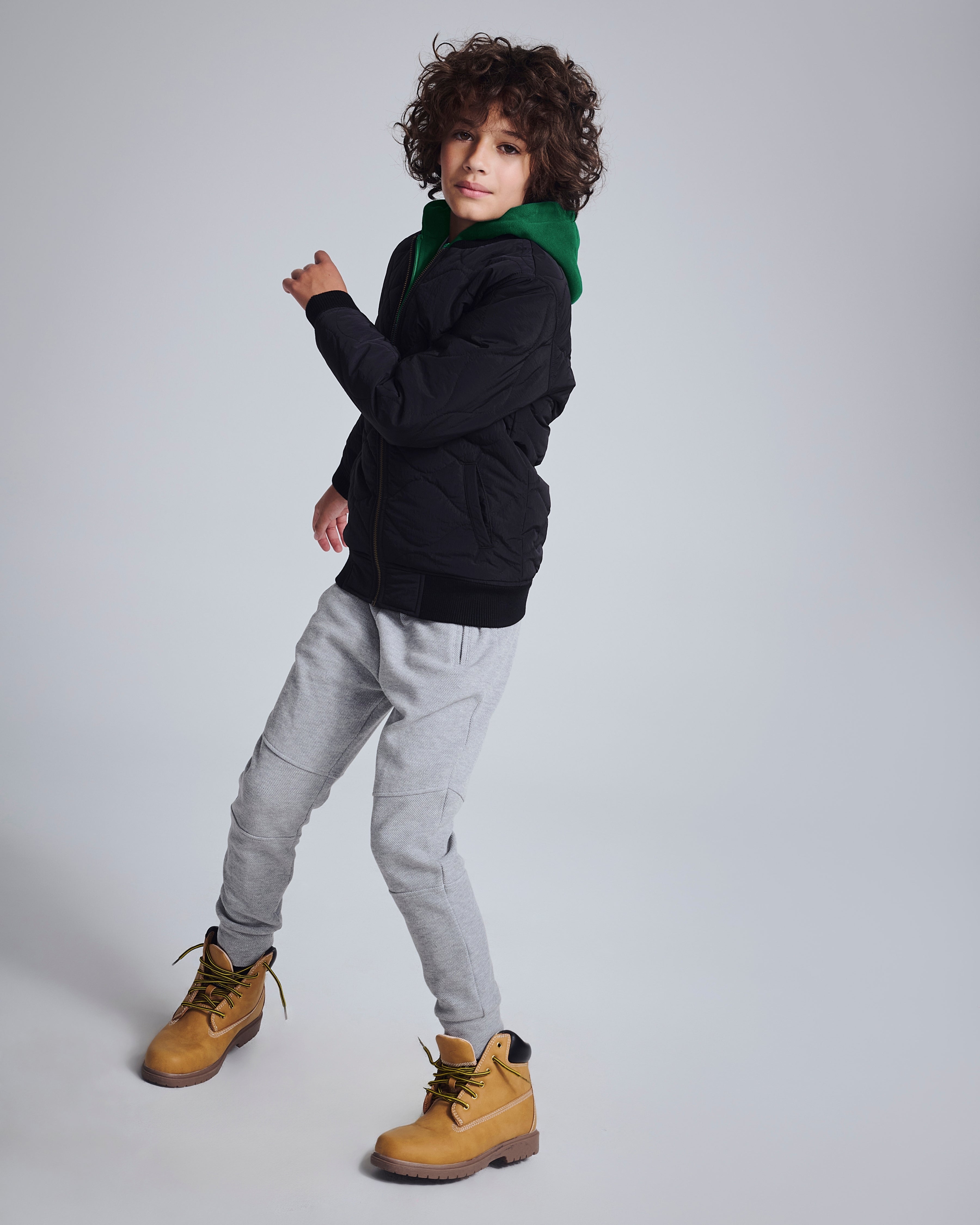 Boy wearing Novelty Grey Heather Sideline Sweatpants with black jacket and yellow boots, stylish and comfortable look.