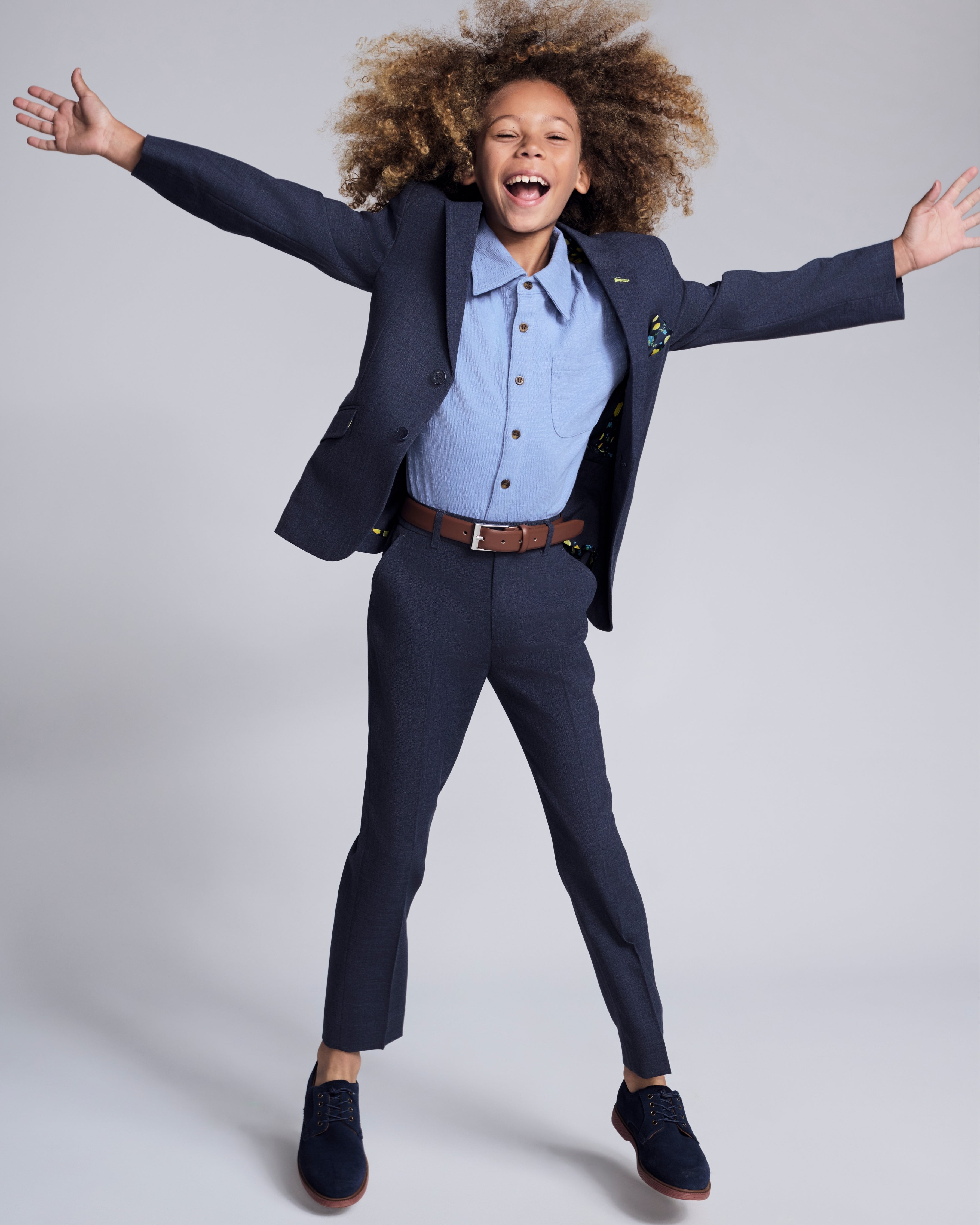 Boy wearing Peacoat Stretchy Mod Suit, smiling and jumping, showcasing modern comfort and style for special occasions.