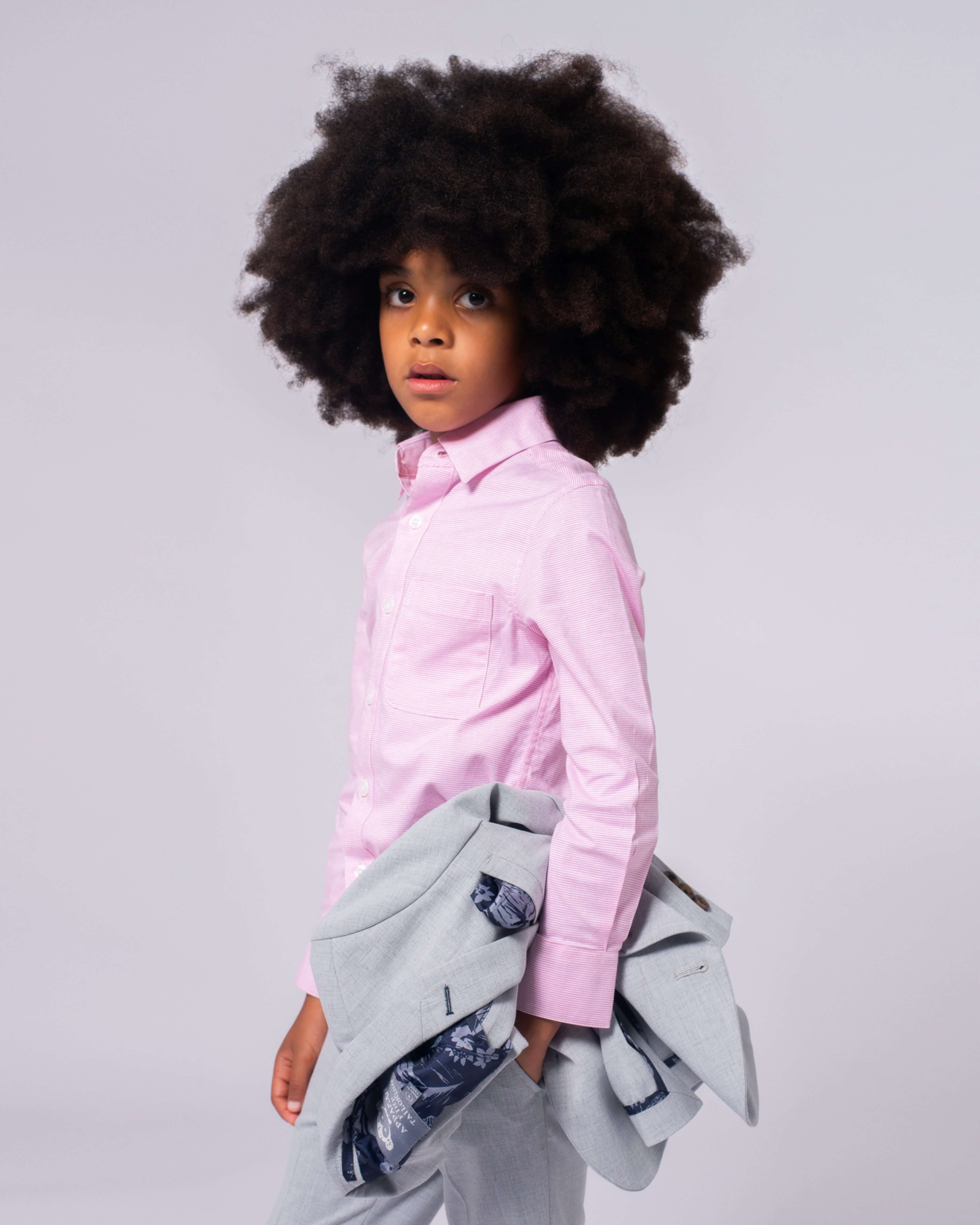 Pink Standard Button Down Shirt worn by a child with curly hair, paired with a stylish outfit and light gray blazer.