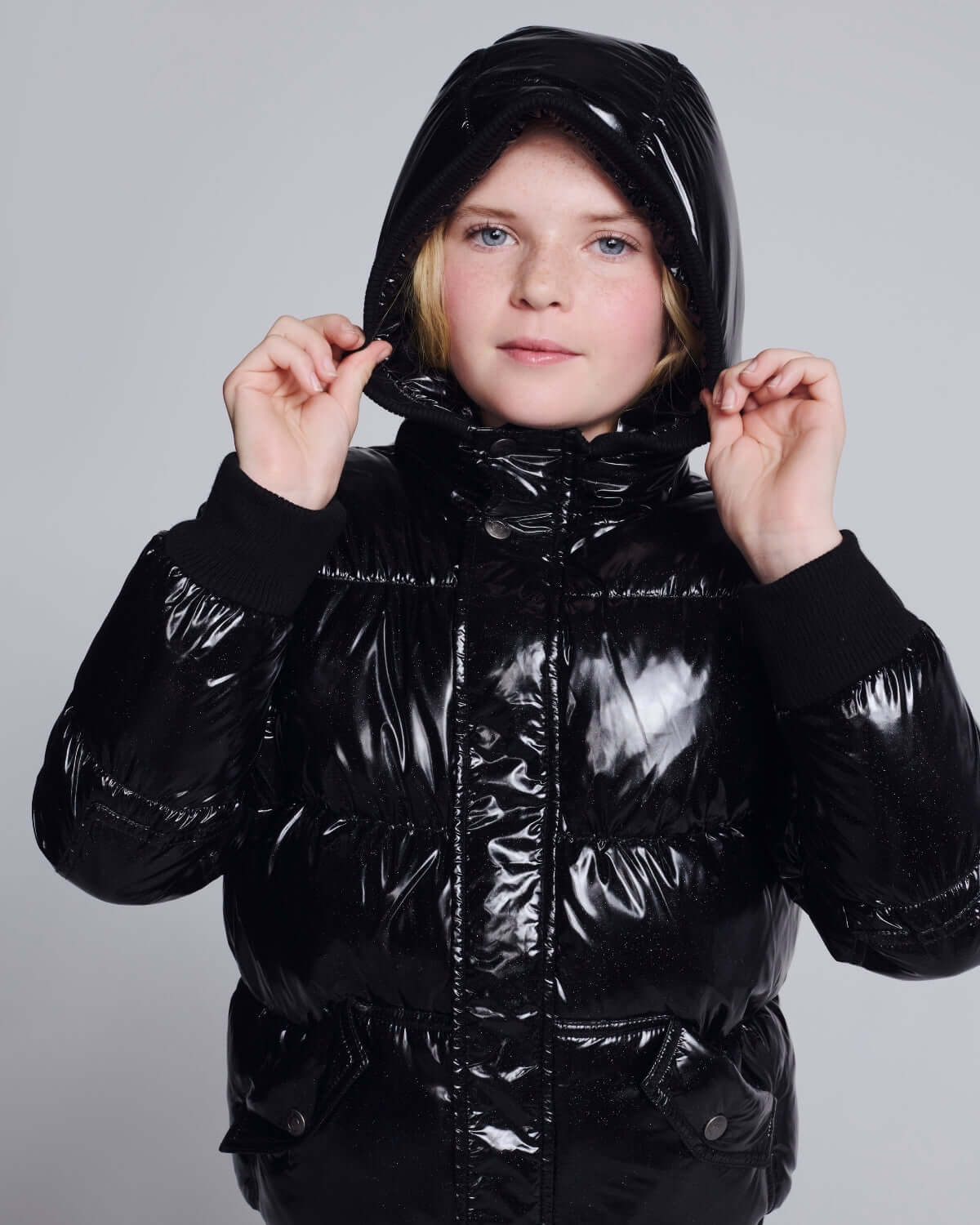 Black Glitter Puffy Coat worn by a girl, featuring a shiny black finish and a hood for warmth and style.