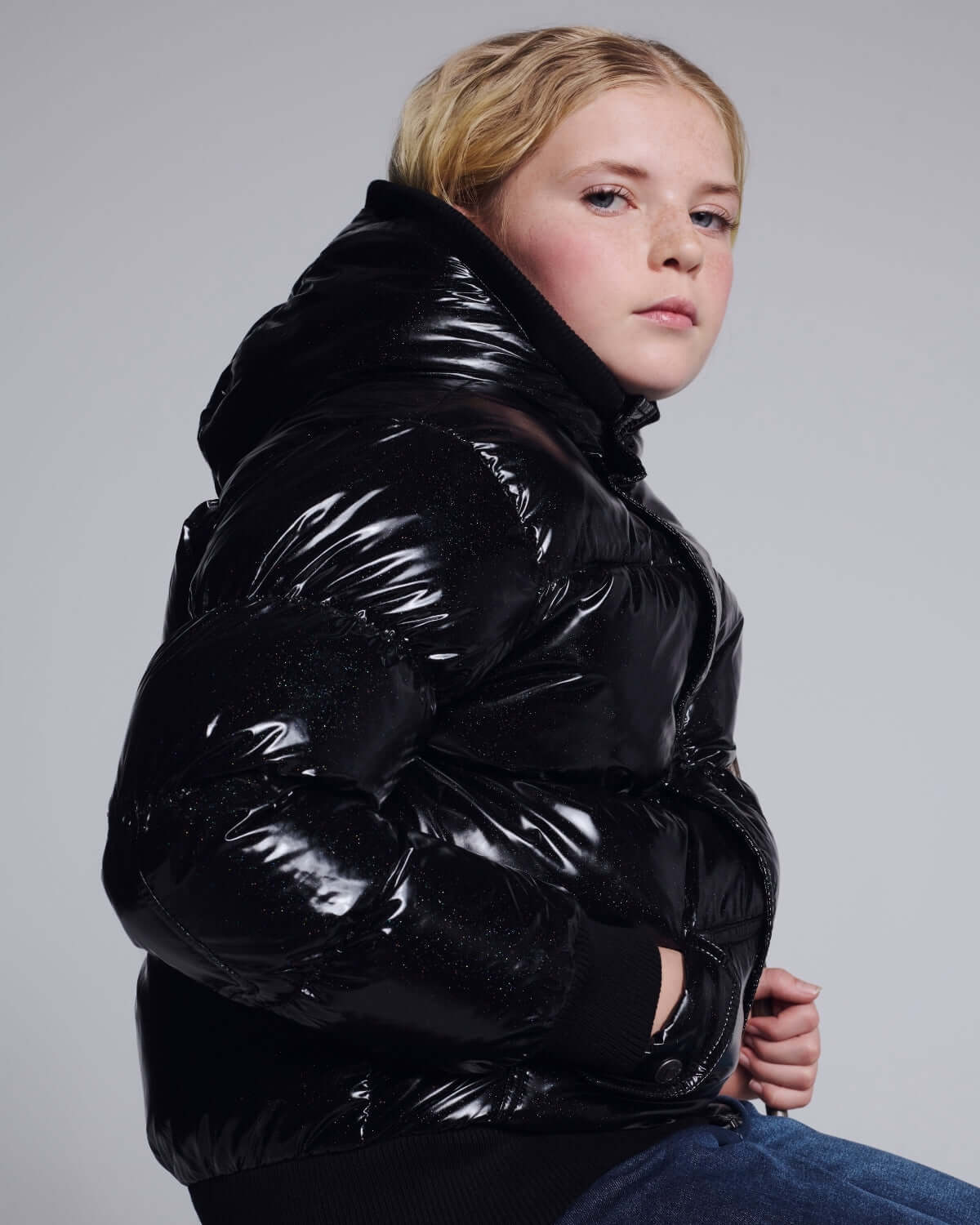 Girl wearing a Black Glitter Puffy Coat showcasing its shiny black fabric and stylish design.