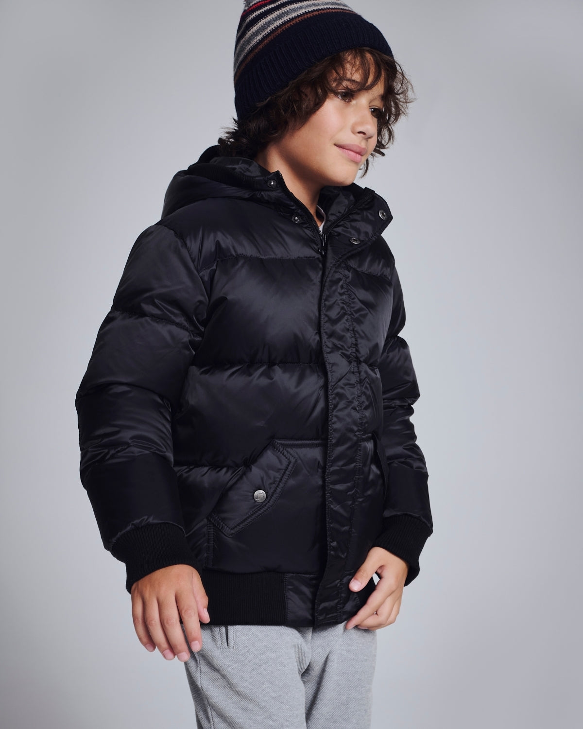 Child wearing a black puffer jacket and gray beanie on a gray background