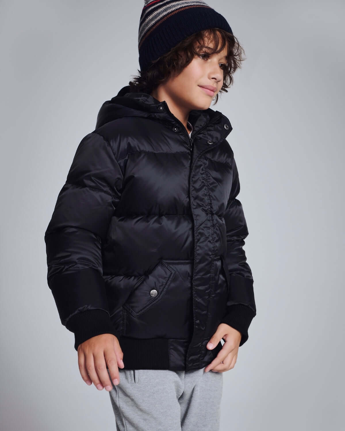 Boy wearing a Black Puffy Coat, featuring a hood and bomber style, perfect for winter outings.