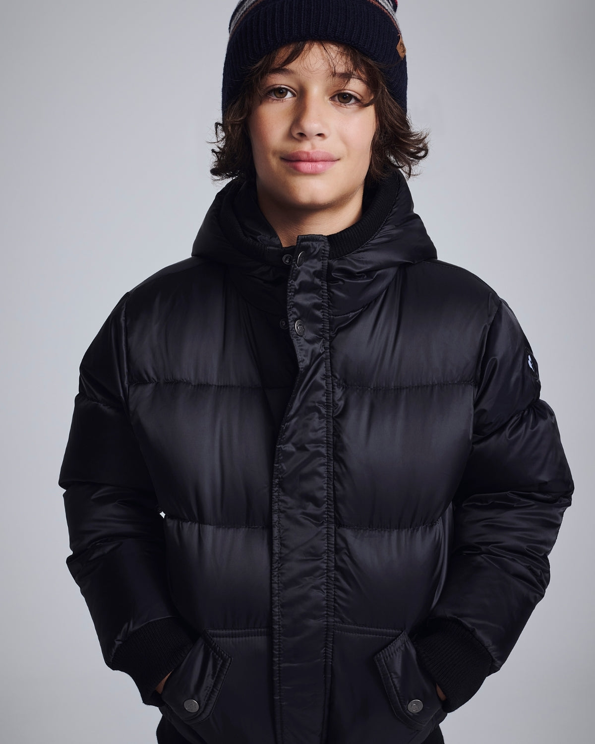 Child wearing a black puffer jacket and beanie against a gray background