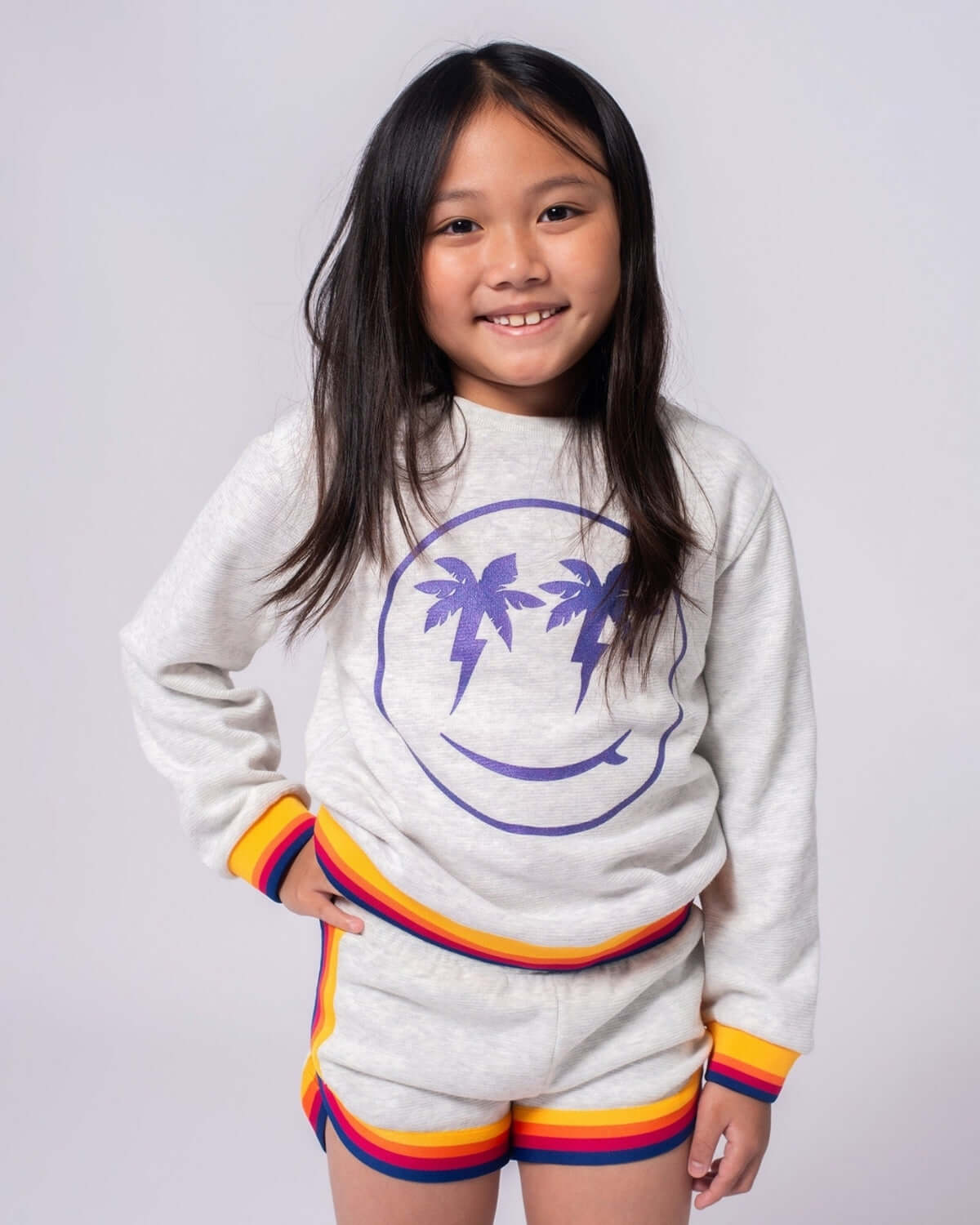 Child wearing Cloud Heather Lori Shorts with a comfy sweatshirt featuring a smiley face and palm trees.