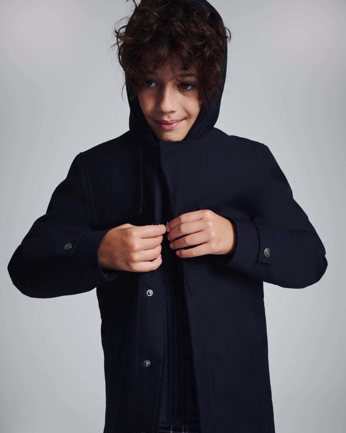 Boy wearing a Navy Blue Urban Gotham Coat with a hood, buttoning it up for a stylish look.