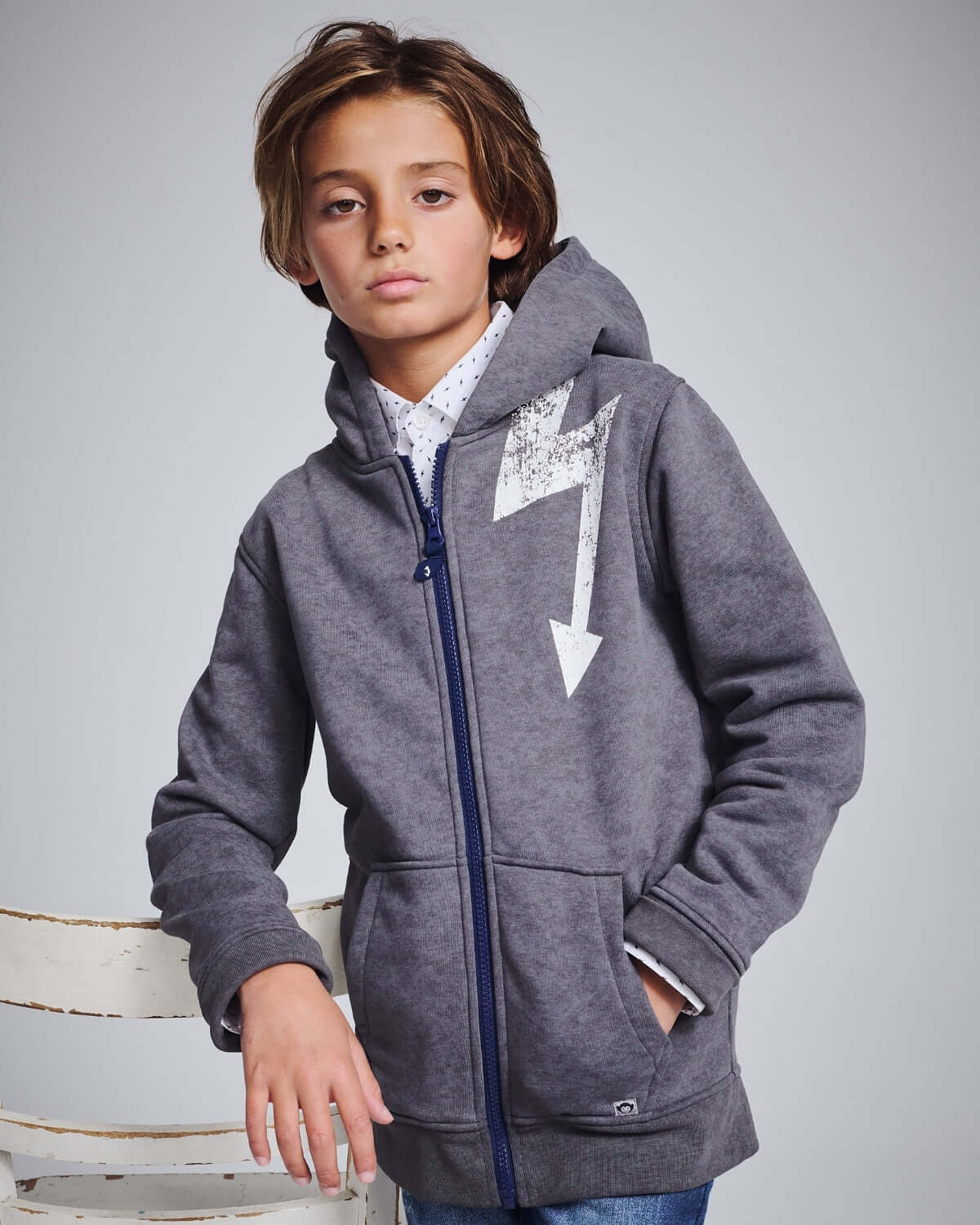 Child wearing a gray hoodie with a white arrow design on a light gray background