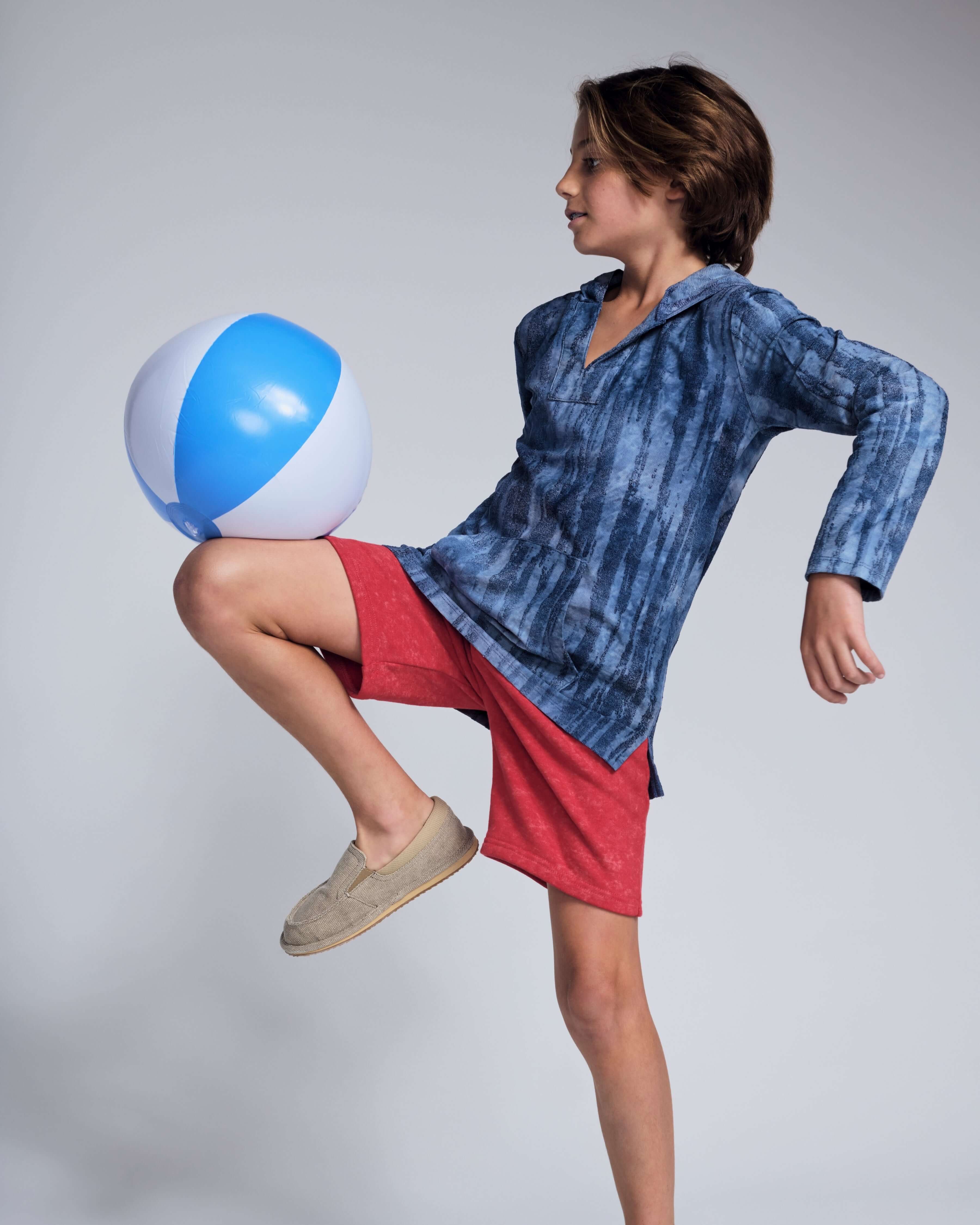 Boy playing with a beach ball while wearing Washed Red Preston Short and a blue hoodie.