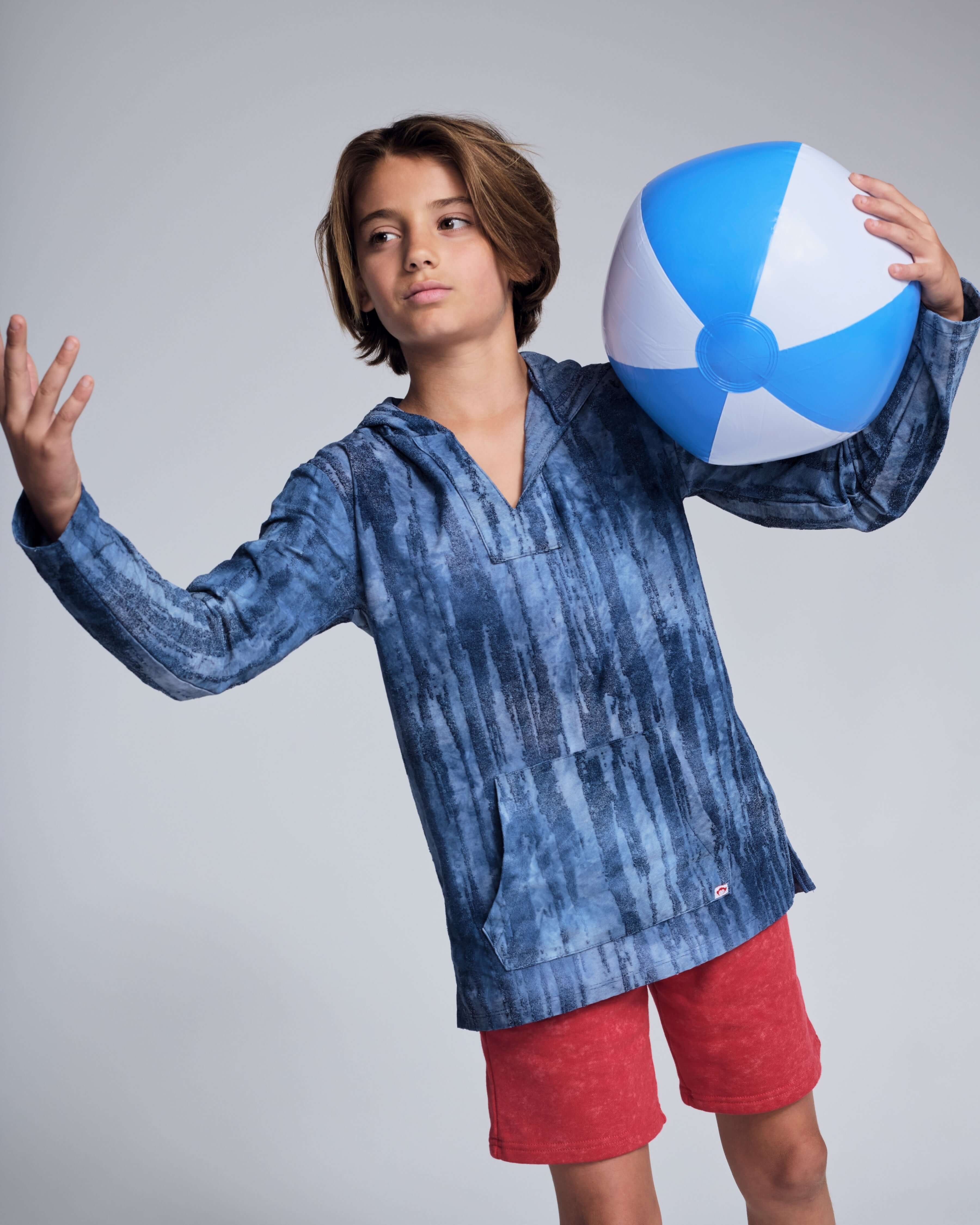 Boy wearing a blue hoodie and Washed Red Preston Short, holding a beach ball, ready for summer fun.