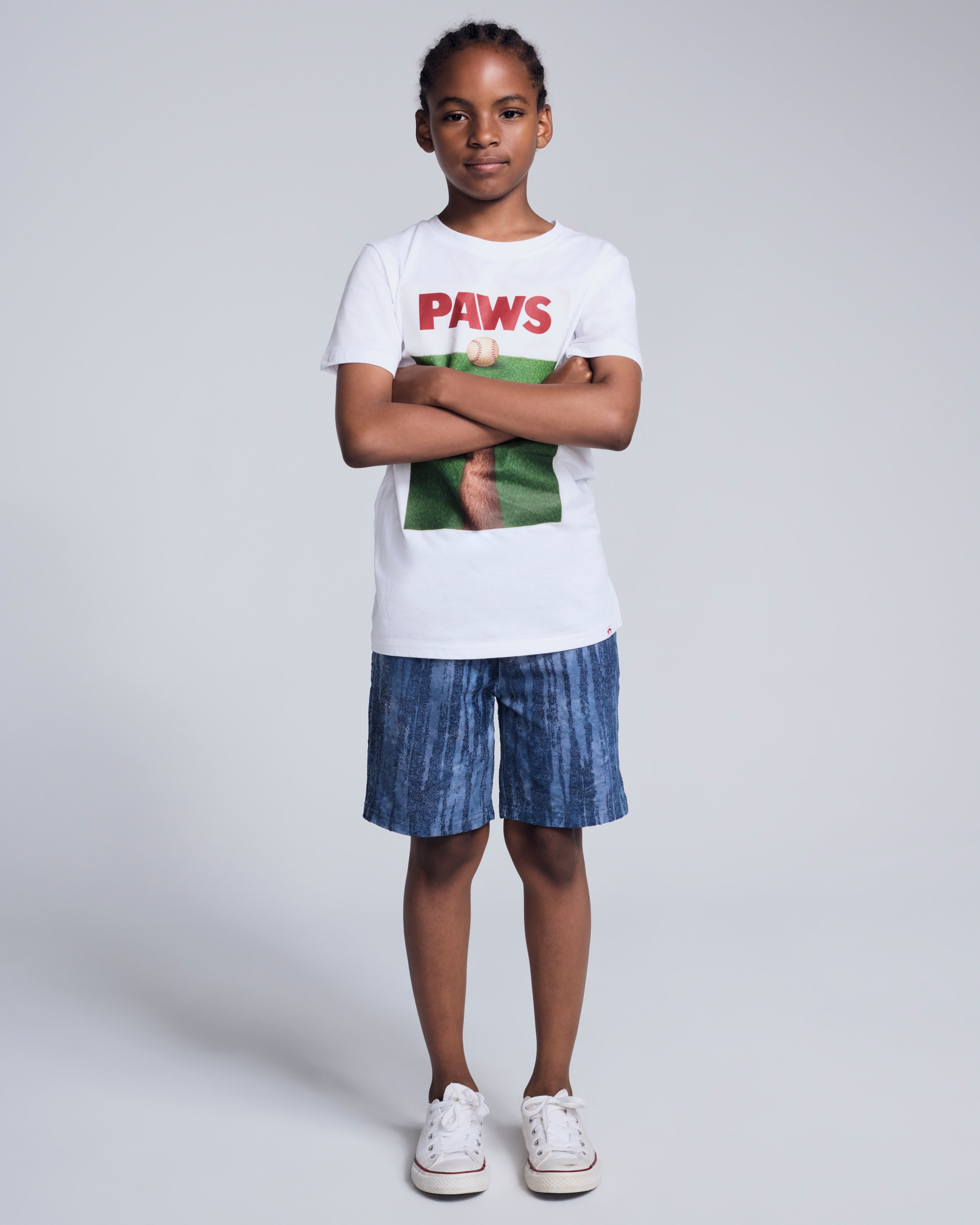 A child wearing a white 'PAWS' graphic t-shirt and Waterfall Preston Short, styled with sneakers.