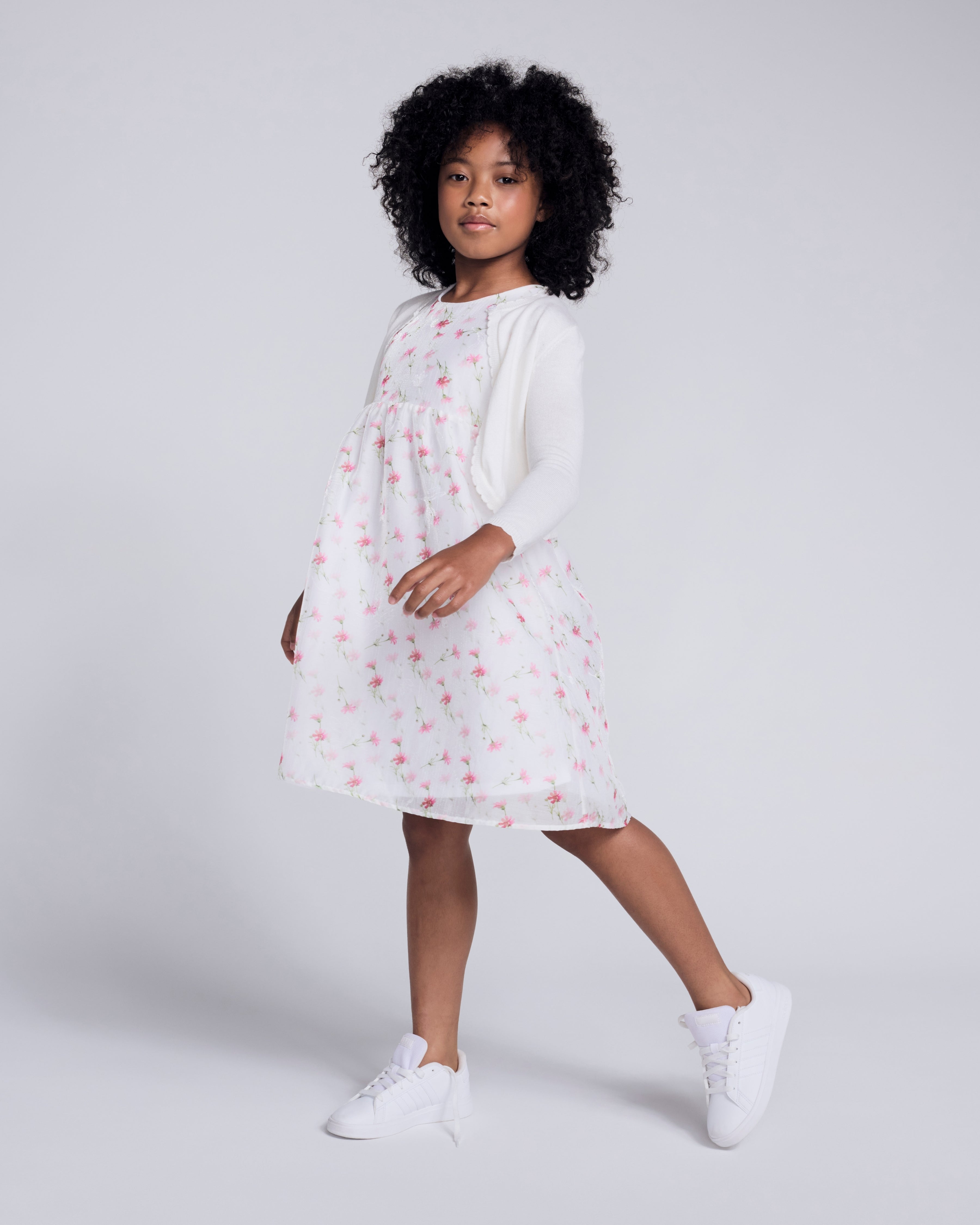 Girl wearing a White Bolero Cardigan over a floral dress, perfect for spring and summer occasions.