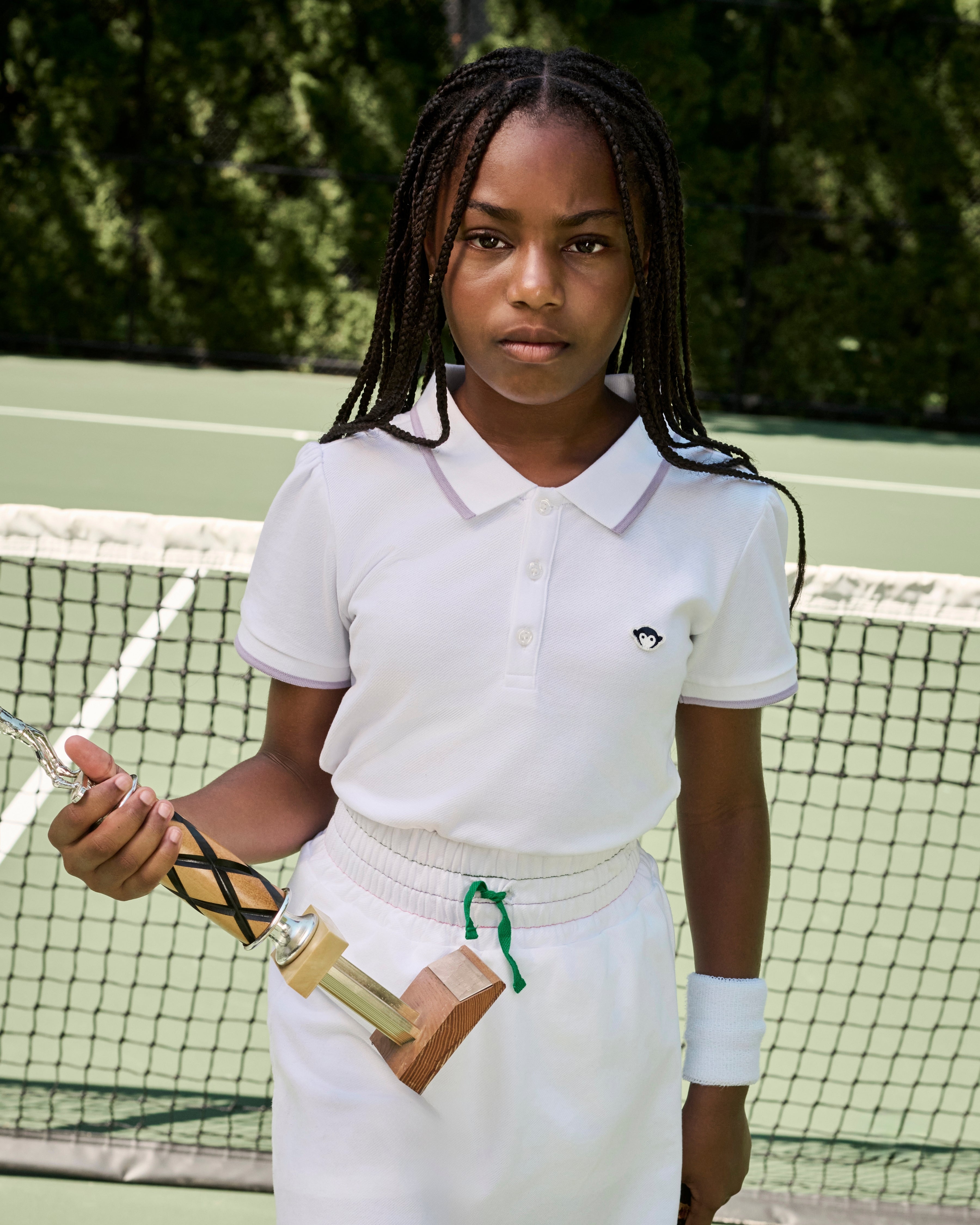 Girl in a white tennis outfit holding a trophy on a tennis court