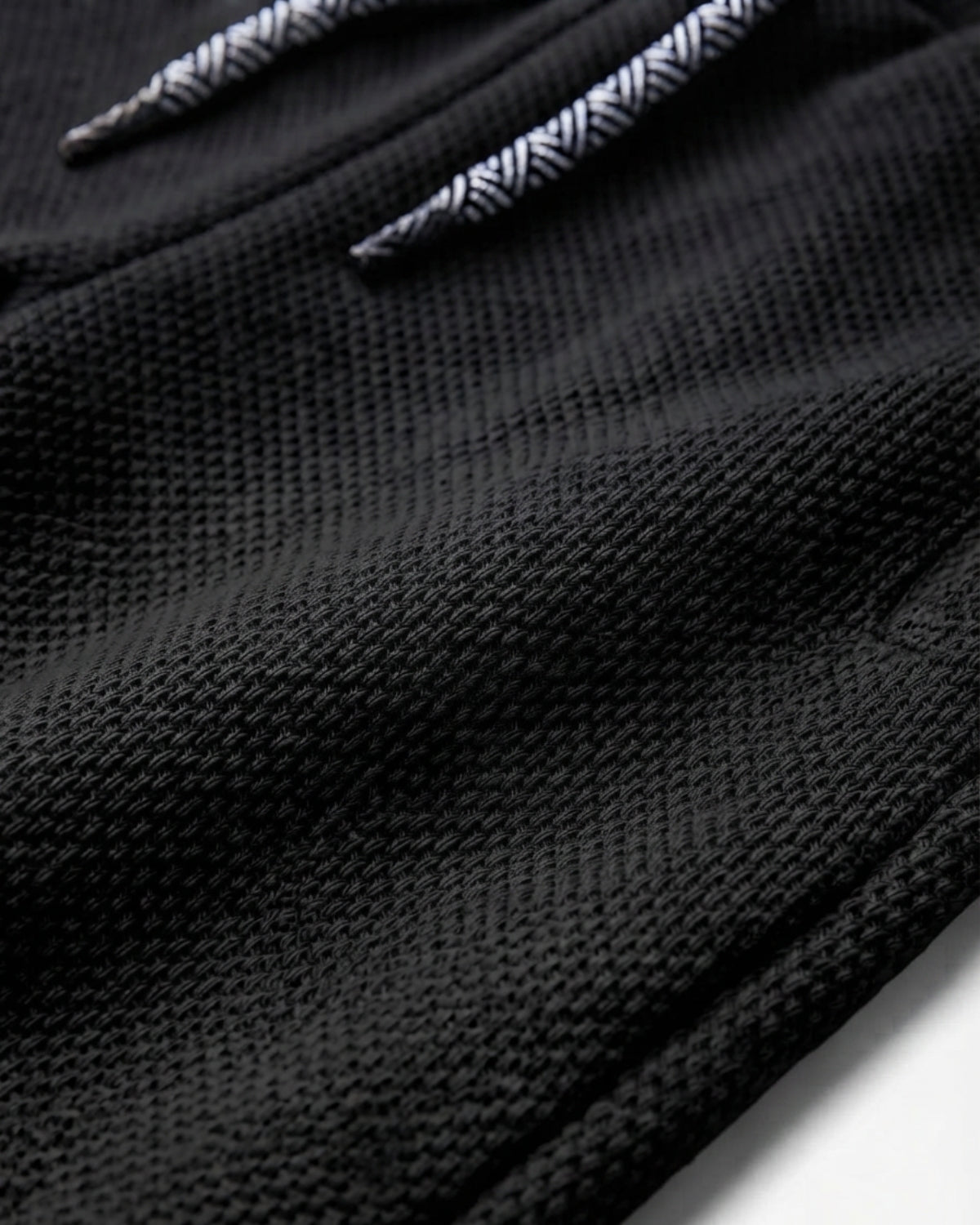 Close-up of a black textured knit fabric with a white and black herringbone patterned drawstring.