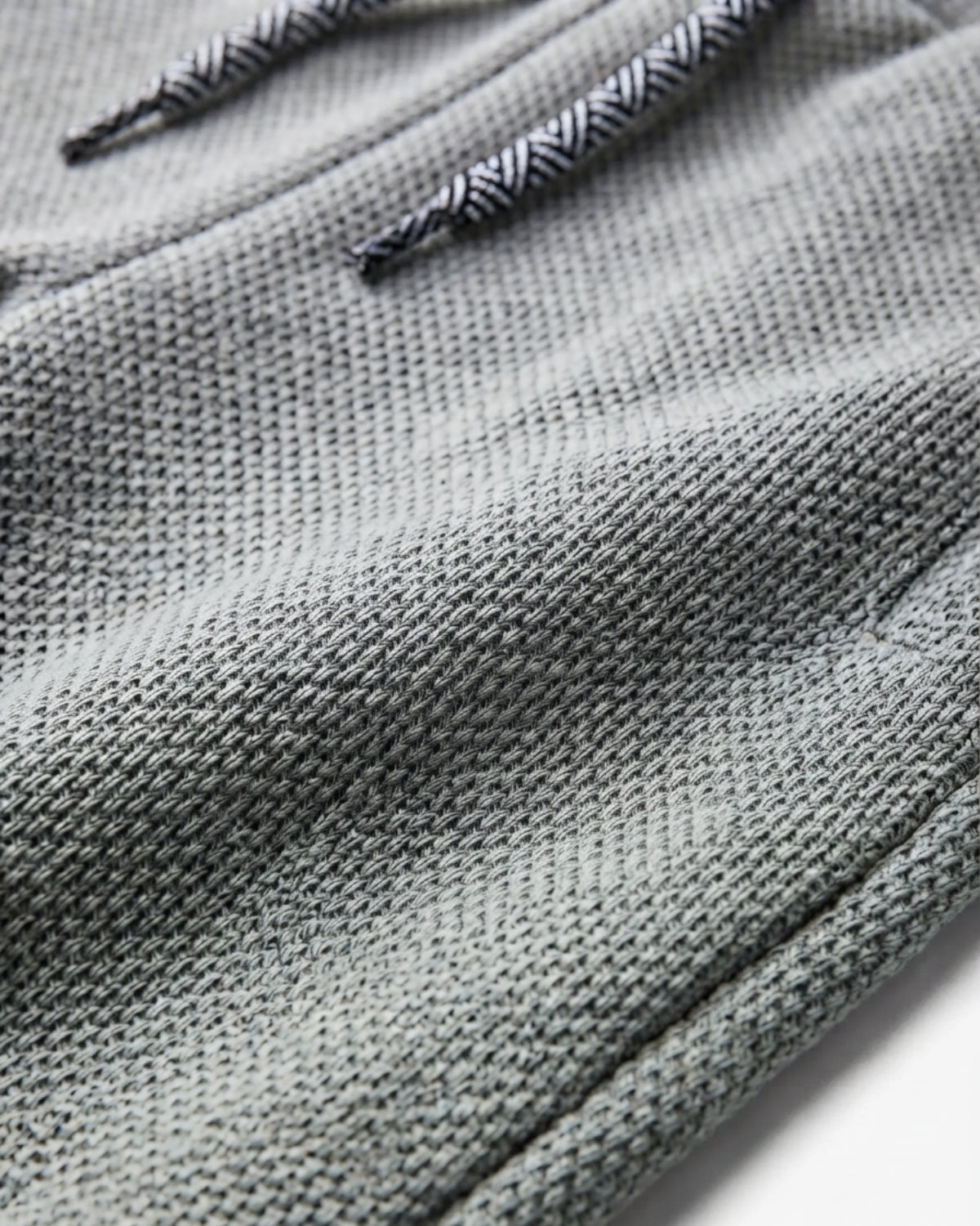 Close-up of a gray textured knit fabric with black and white patterned drawstrings.