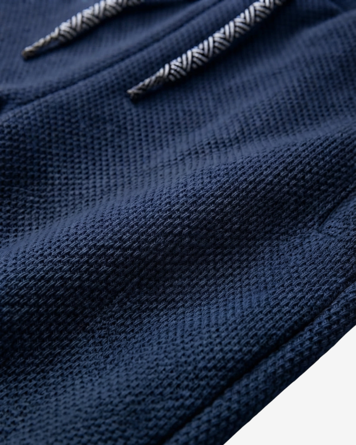 Close-up of a navy blue textured knit fabric with a white and gray herringbone patterned drawstring.